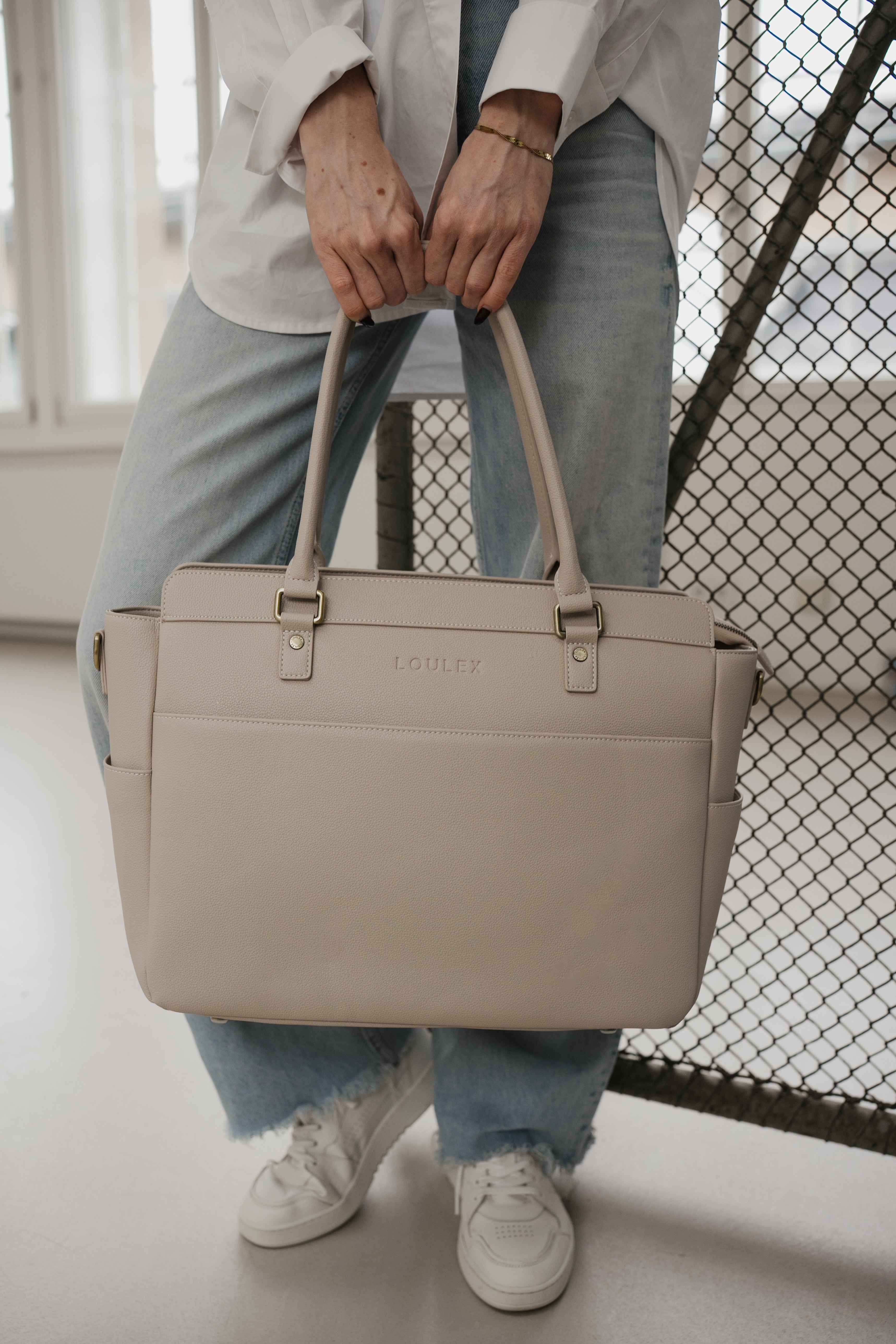 Person holding a beige handbag with a neutral background