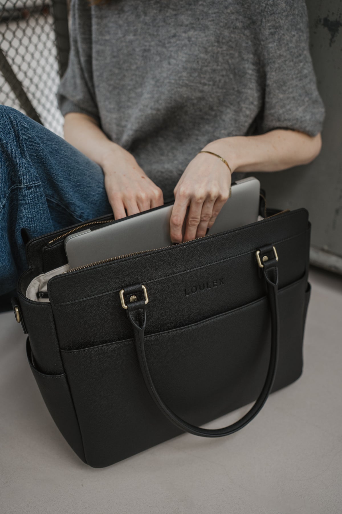 Person holding a black laptop bag with a gray laptop inside, sitting on a bench.