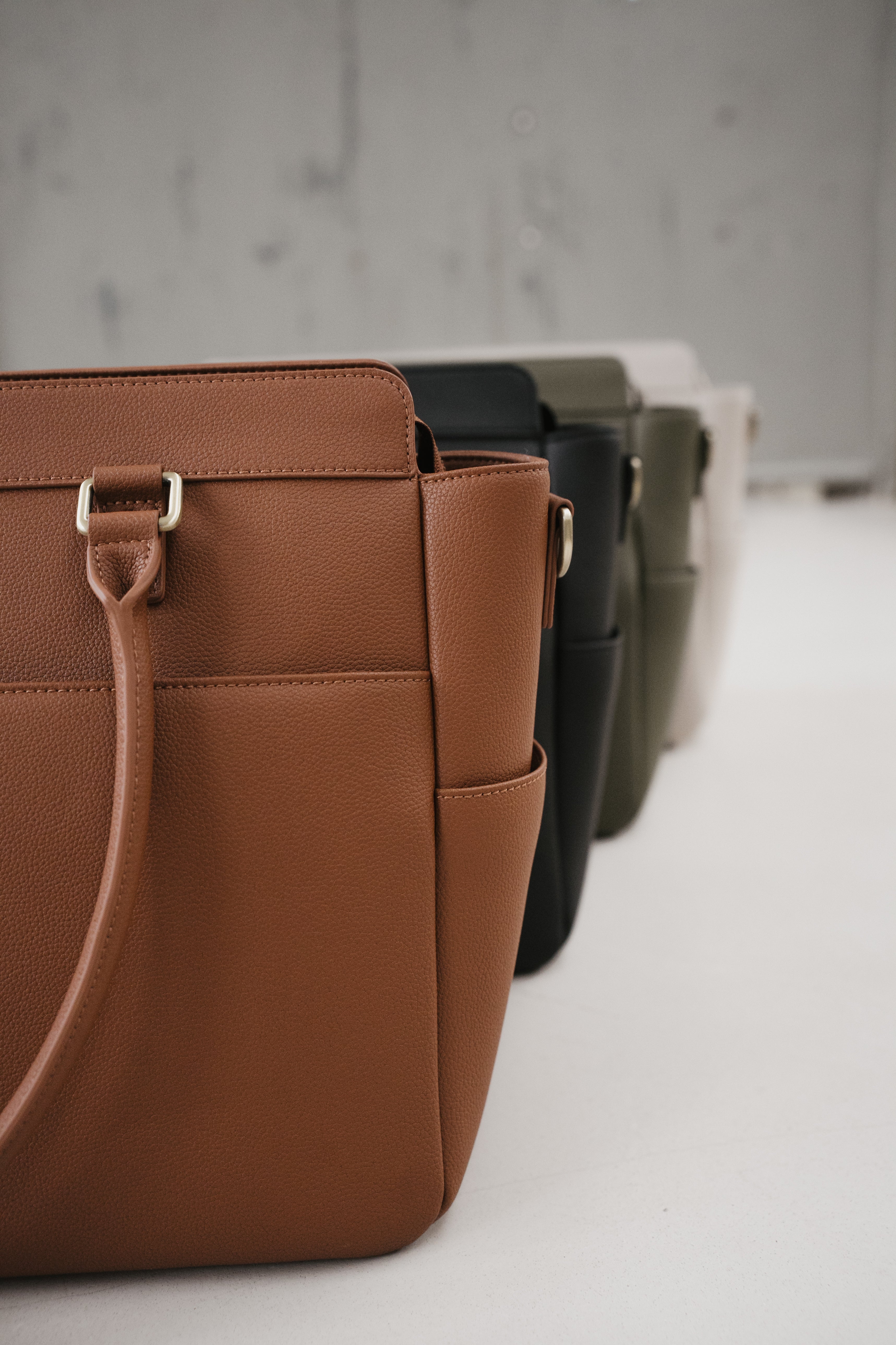 Brown leather handbag with other bags in the background on a light surface.