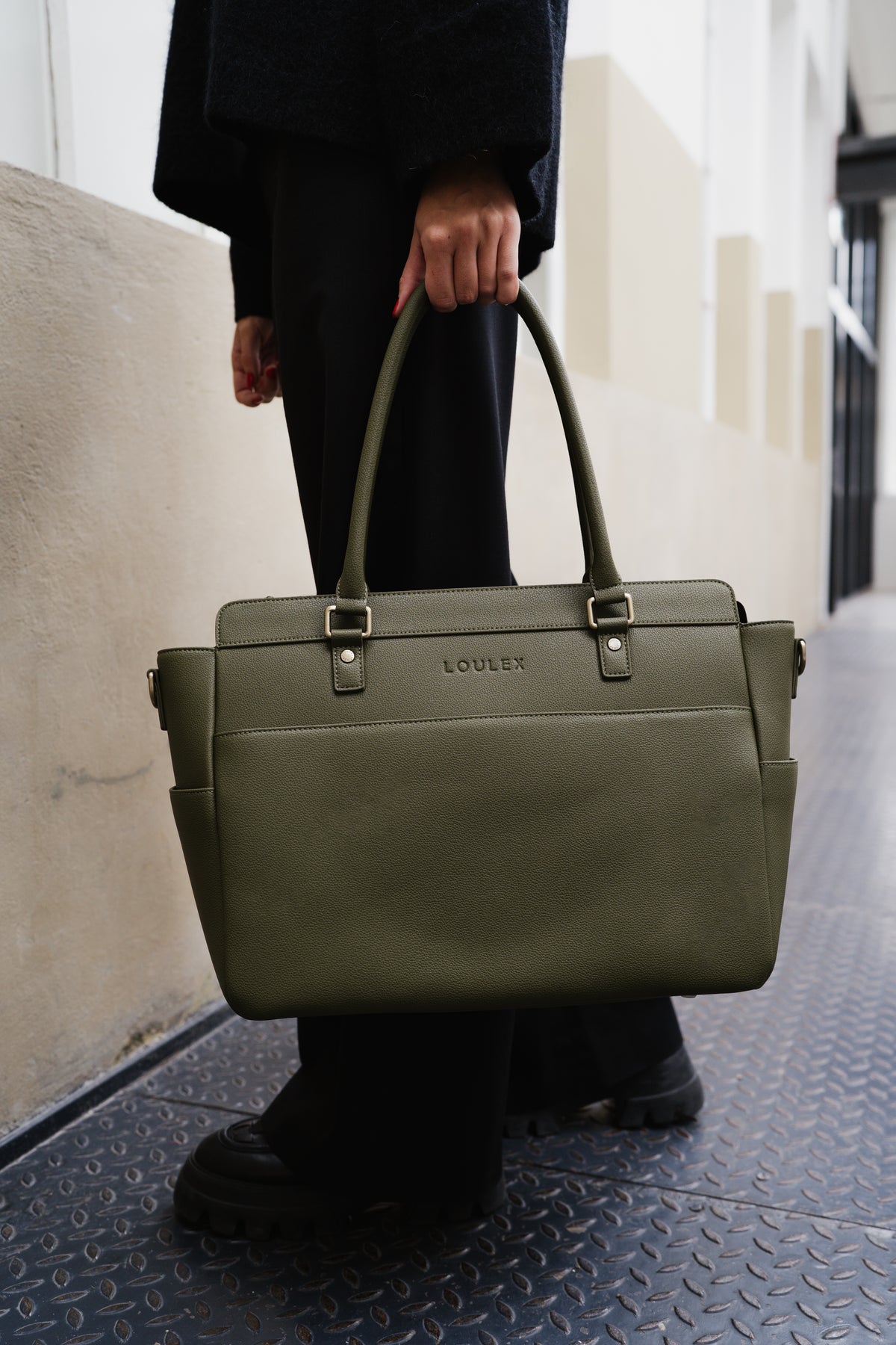 Person holding a green leather bag with 'LOEWE' branding on a city street.