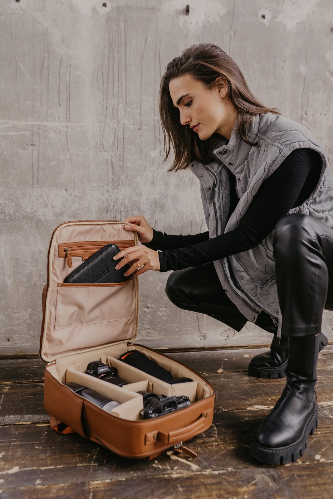 Woman organizing a brown suitcase with compartments on a wooden floor.