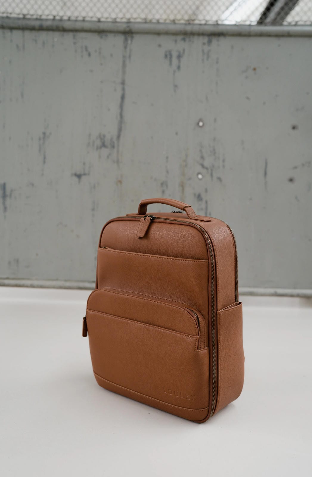 Brown leather backpack on a light gray surface with a textured wall background