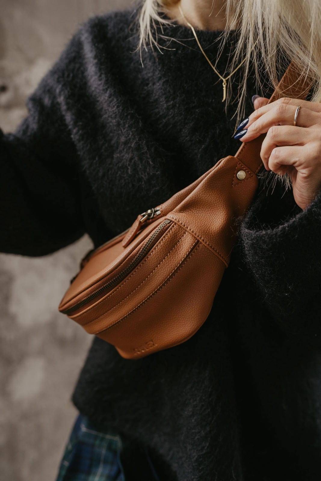 Person wearing a dark sweater holding a brown leather bag against a neutral background