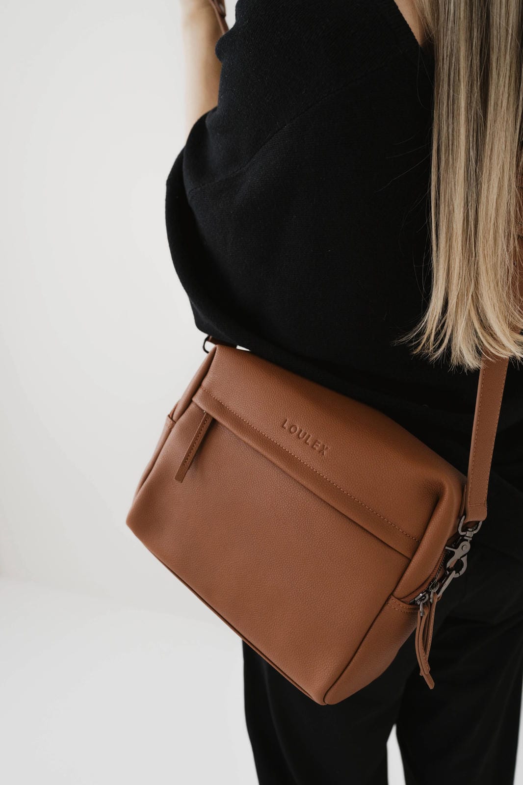 Brown handbag with visible brand logo worn by a person on a white background