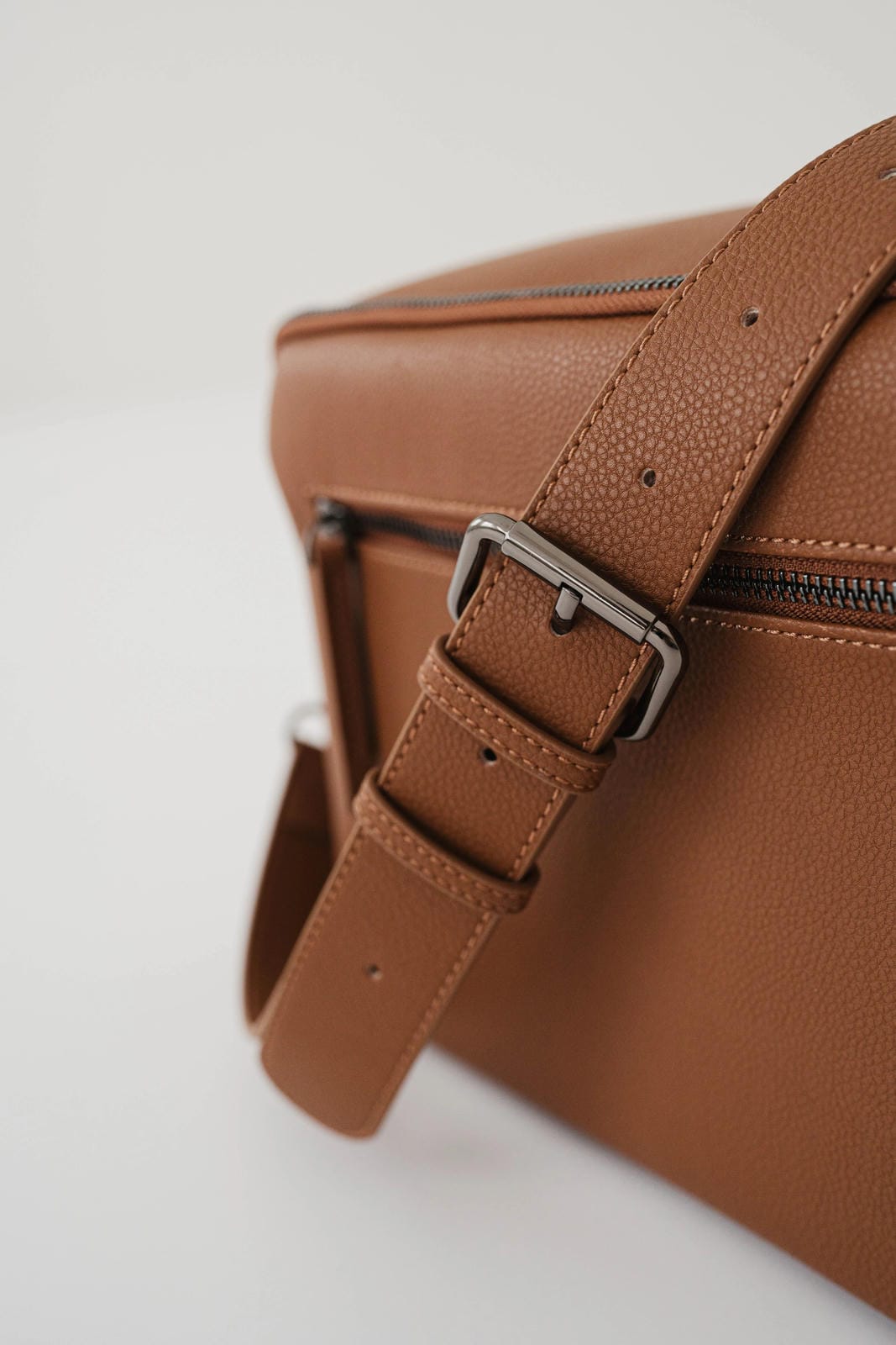 Brown leather bag with a strap and buckle on a light background