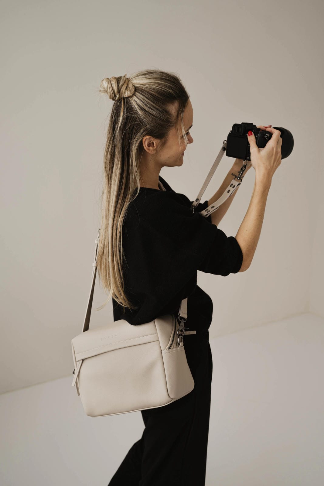 Person holding a camera with a beige handbag on a plain background