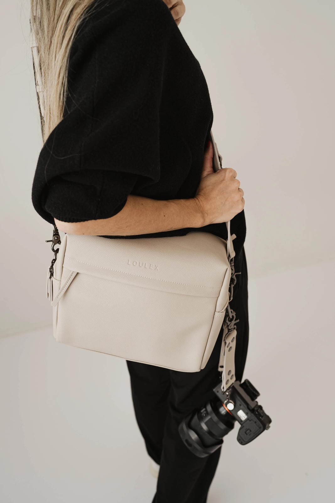 Person holding a beige bag with a visible brand logo against a plain background