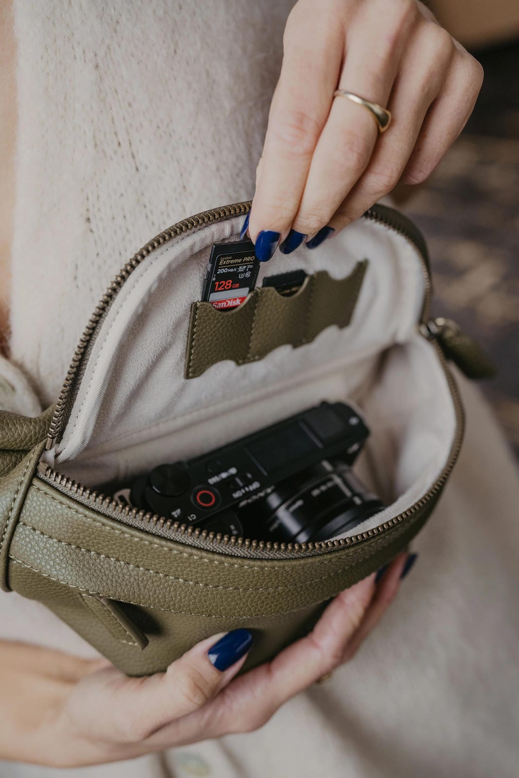 Person opening a small beige bag to reveal electronic devices inside.