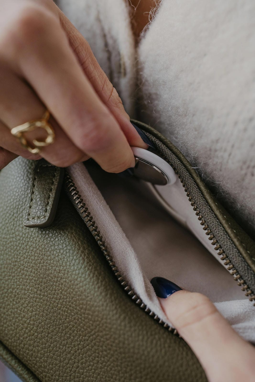 Close-up of a hand opening a green leather bag with a gold ring on a blurred background