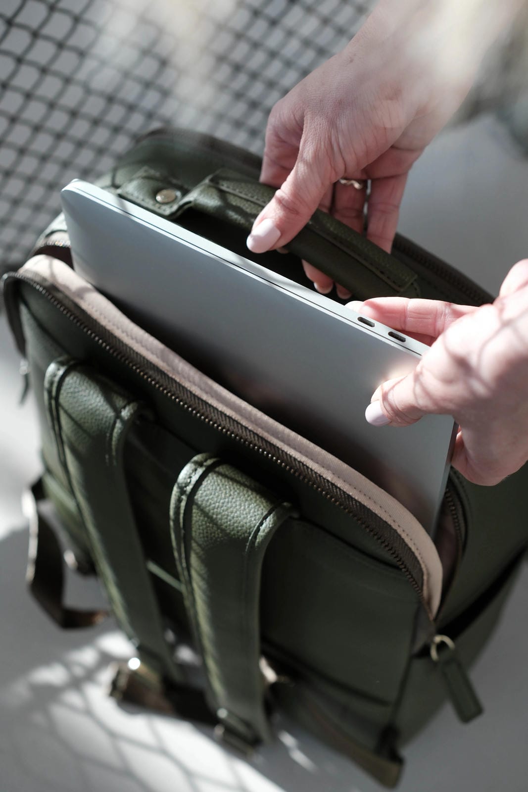 Person placing a laptop into a green leather briefcase.