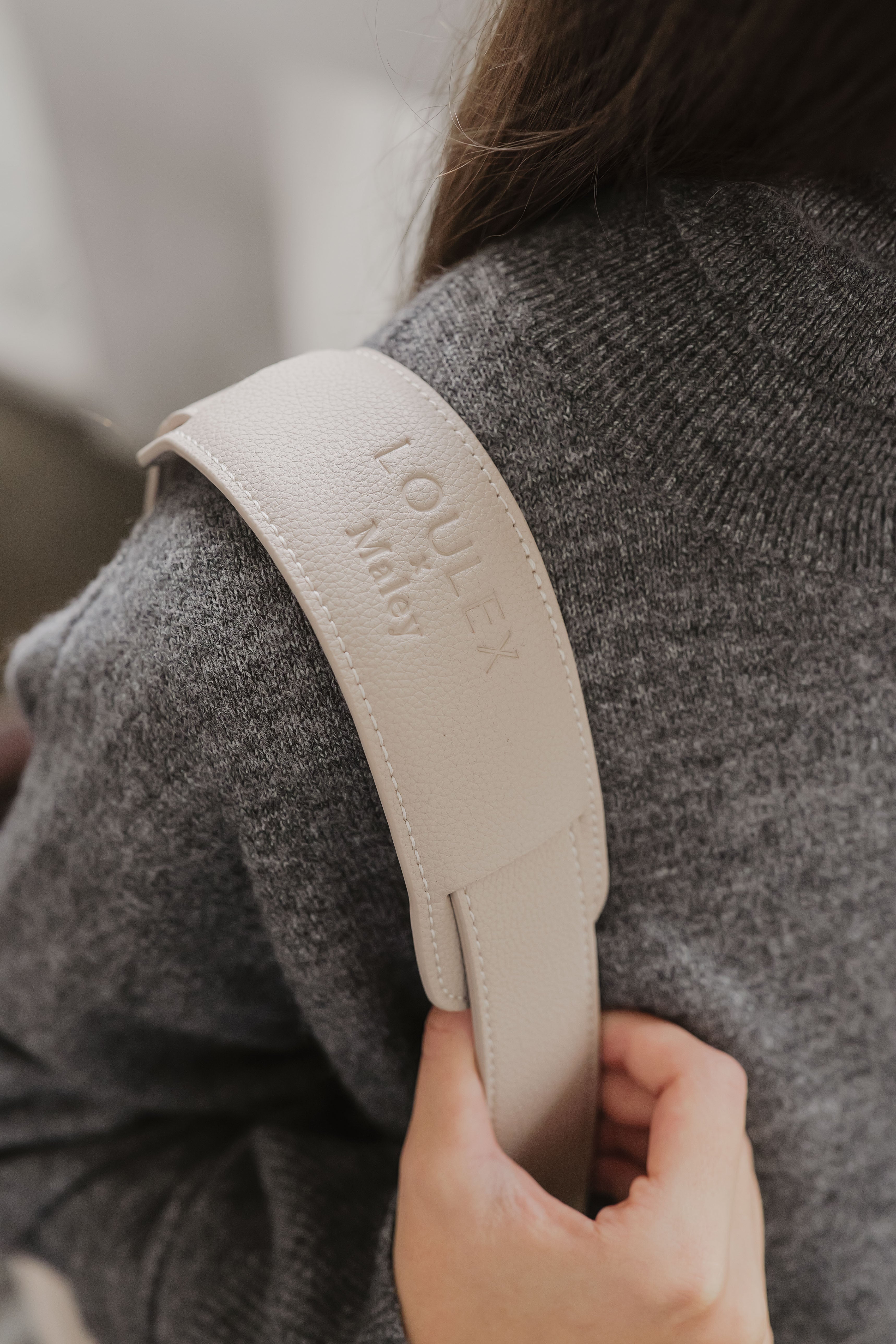 Beige strap with 'LOULEX' branding held by a person wearing a gray sweater.