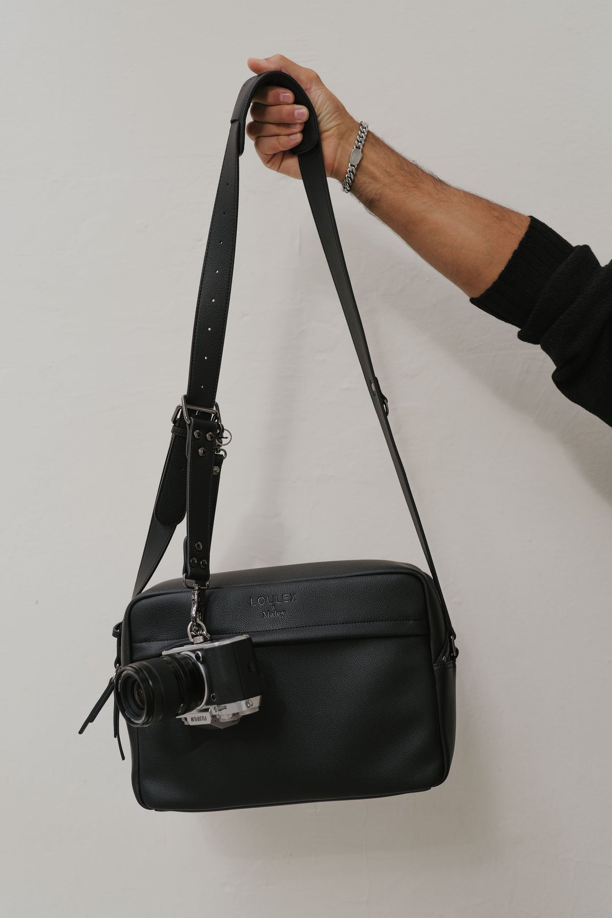 Black leather bag held by a hand against a plain background