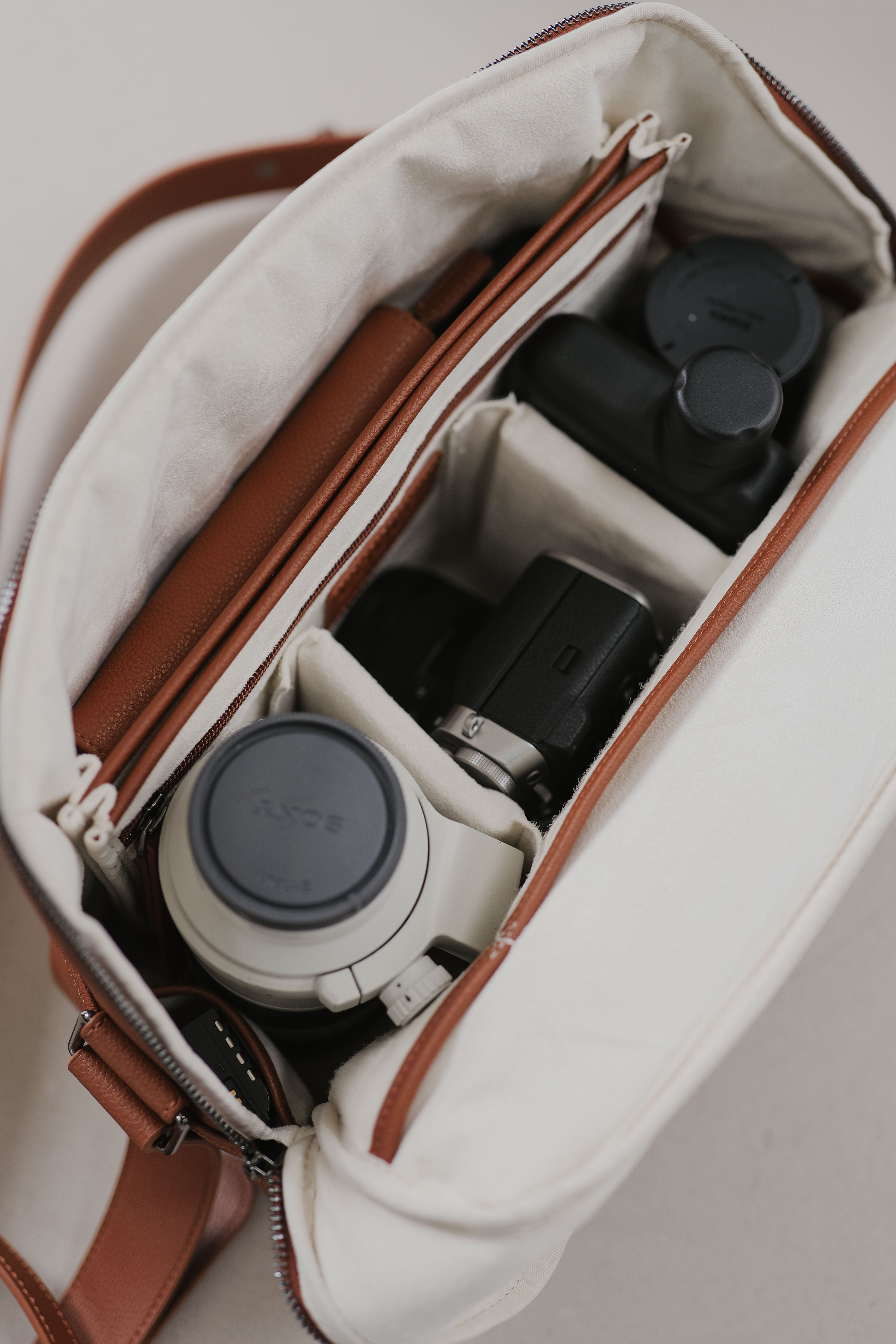 Camera equipment inside a white bag with brown straps on a light gray background