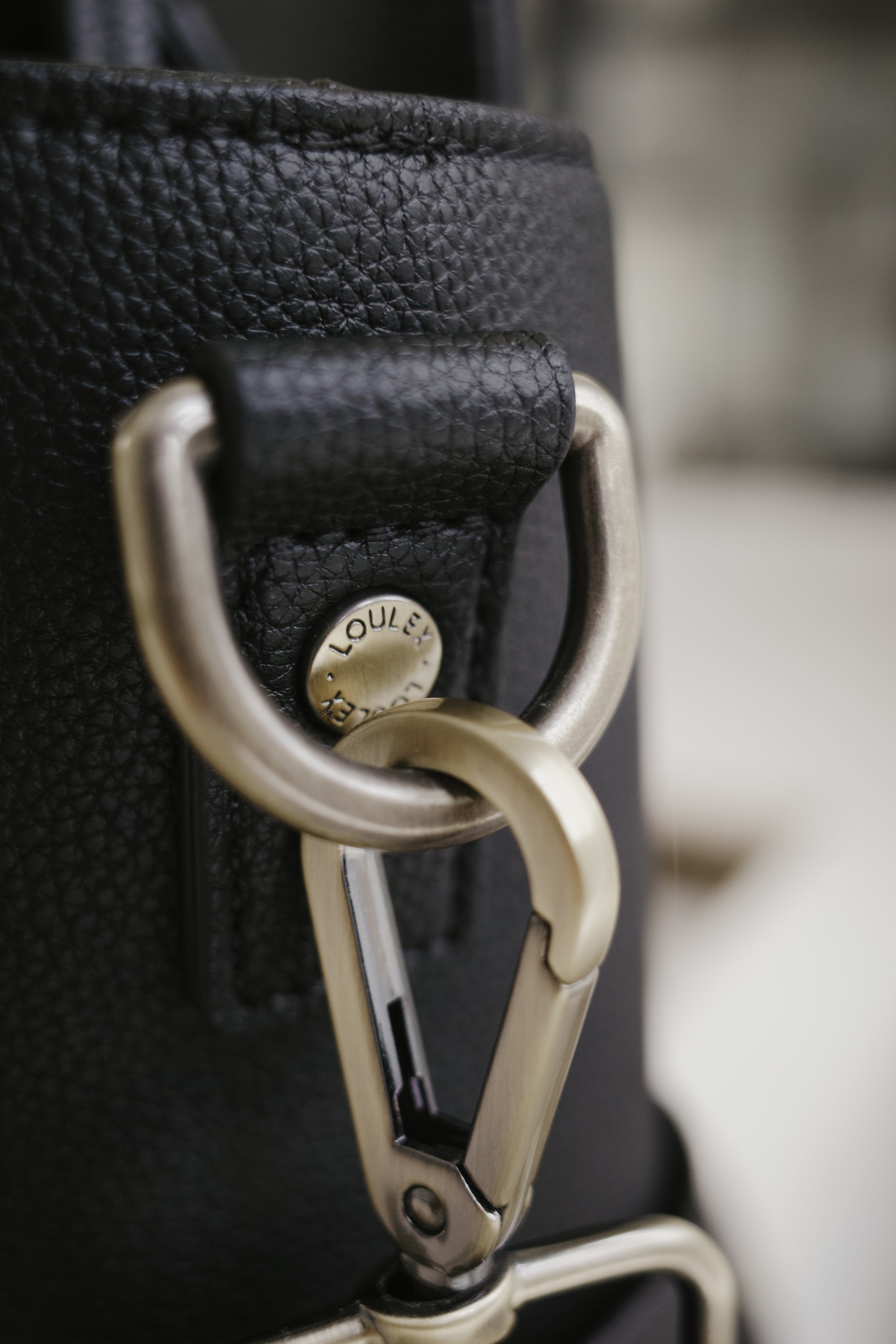 Close-up of a black leather bag with a gold carabiner and 'Louis Vuitton' logo.