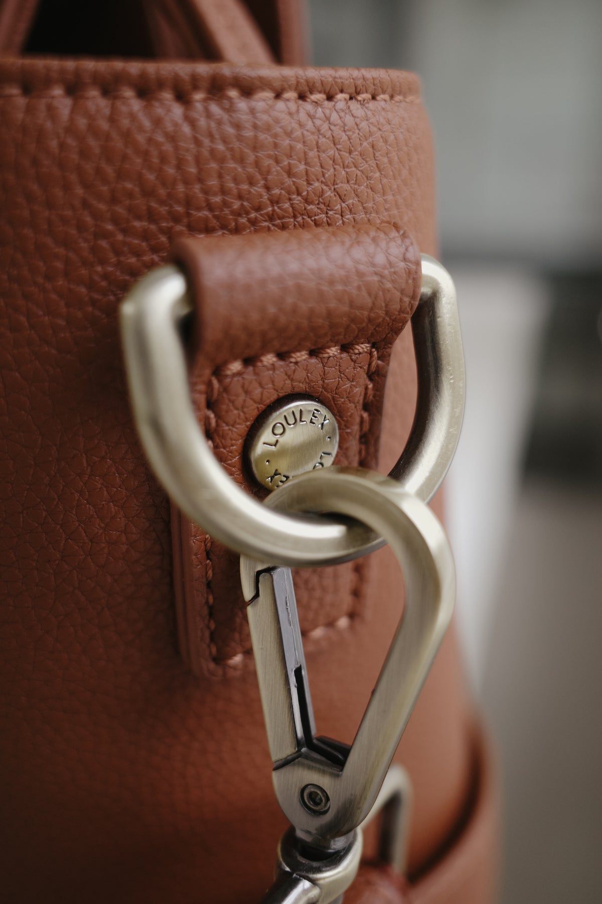 Close-up of a brown leather bag with a metal carabiner attachment.
