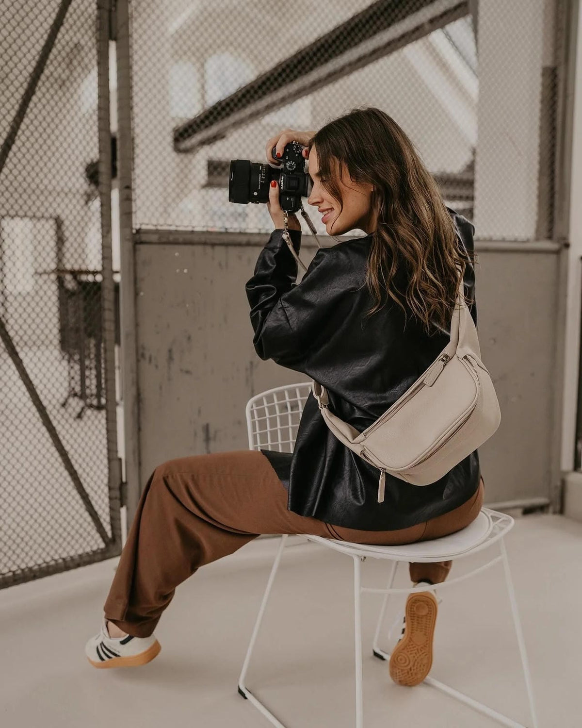 Woman taking a photo with a camera, sitting on a chair outdoors.
