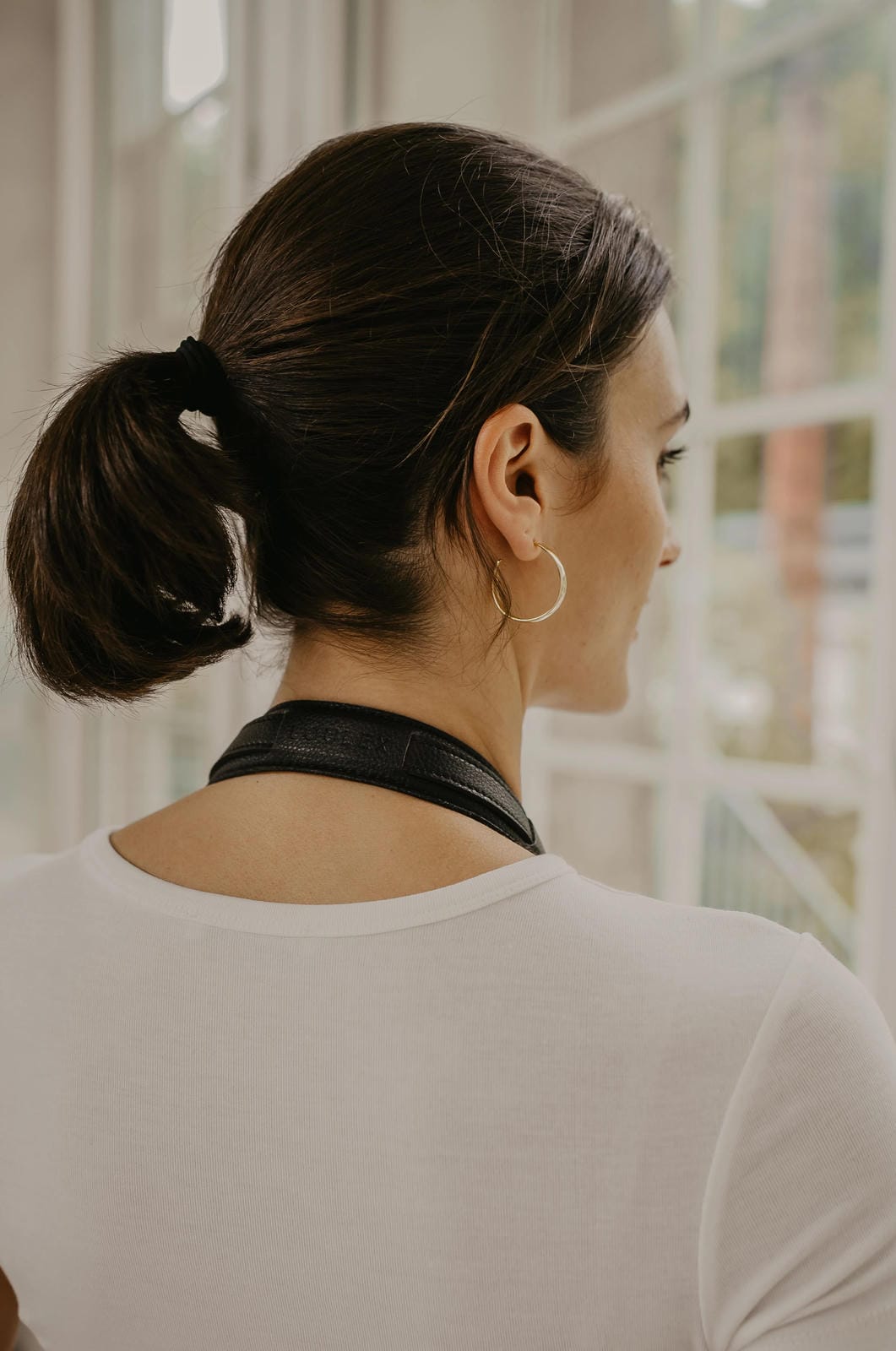 Woman with a ponytail wearing a black choker in front of a window.