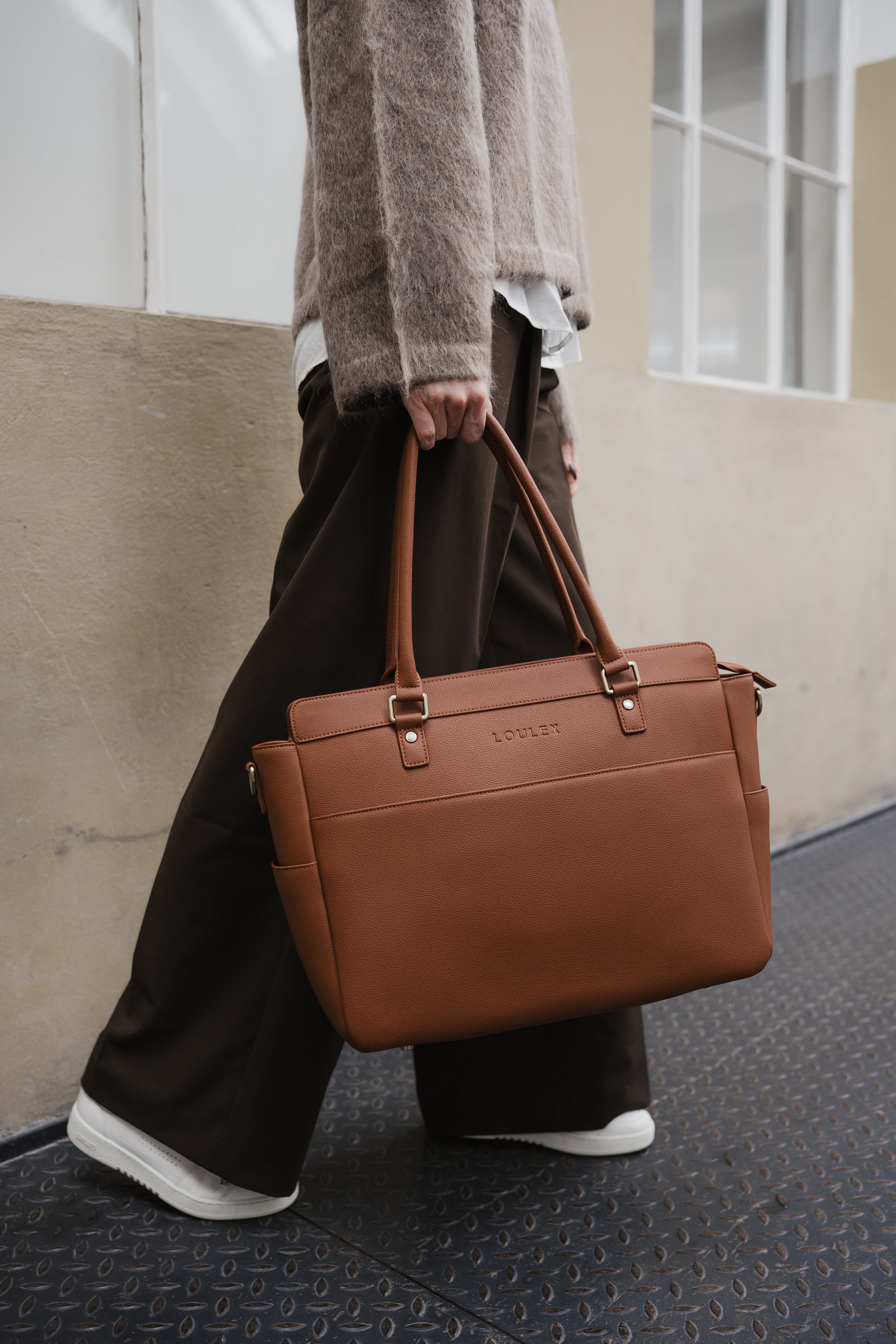 Person holding a brown leather bag with a neutral background