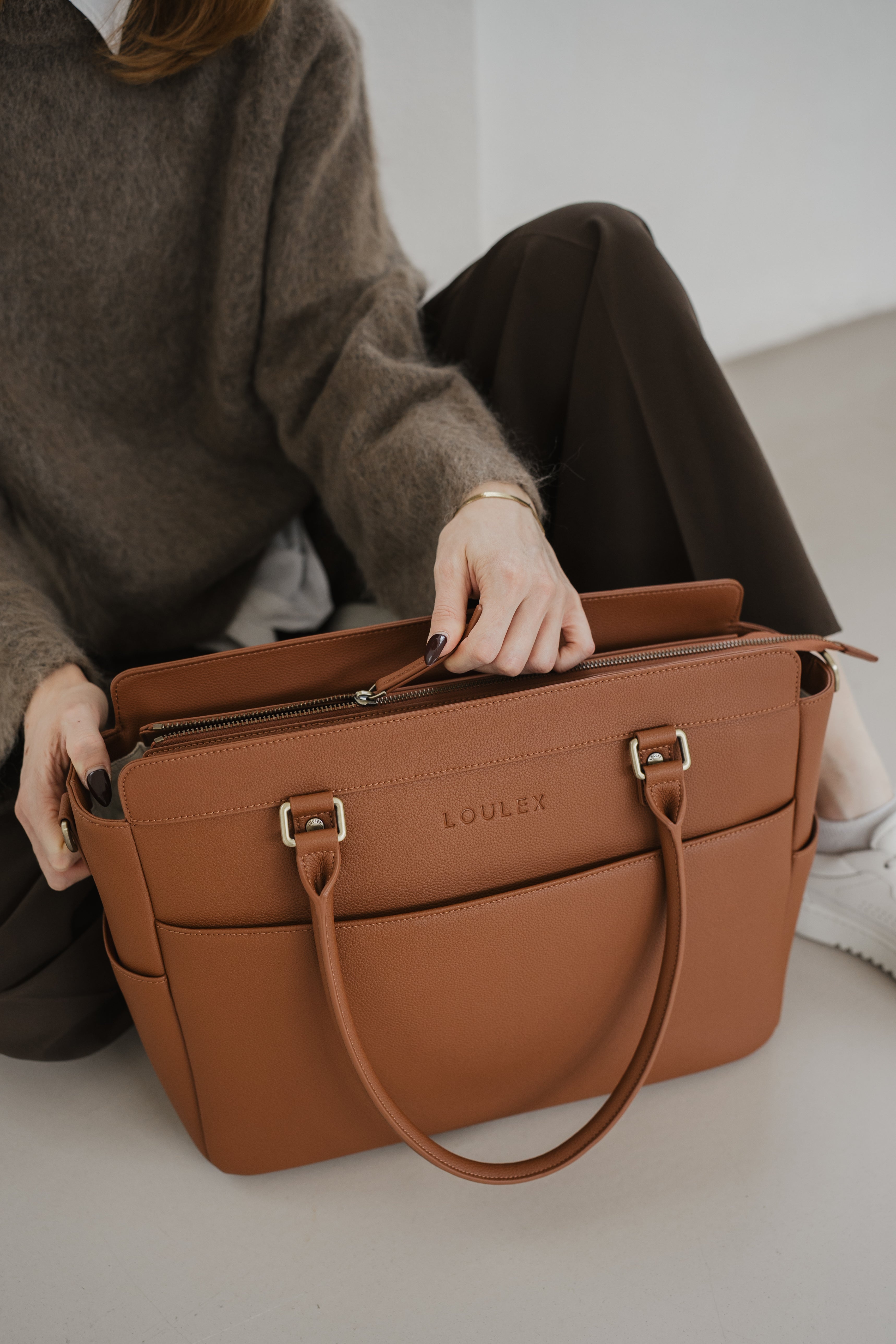 Person holding a brown leather bag with 'LOULOU' branding on a light background