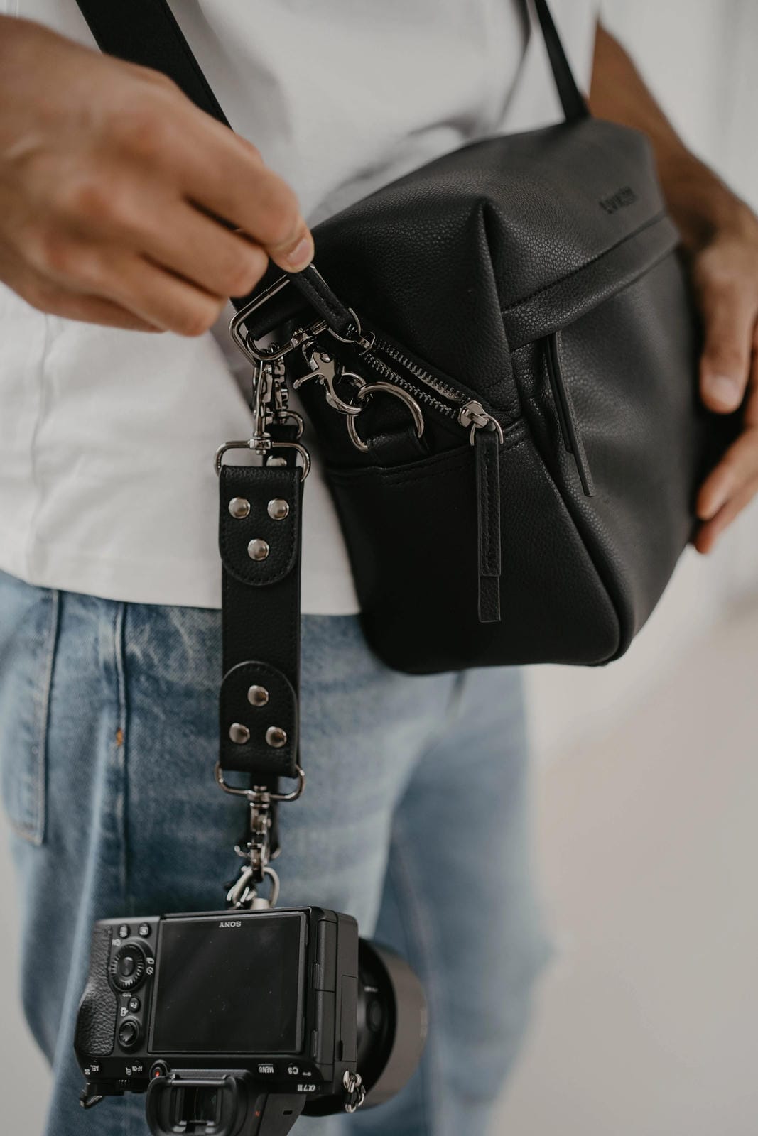 Person holding a black camera bag with a camera attached, wearing a white shirt and blue jeans.