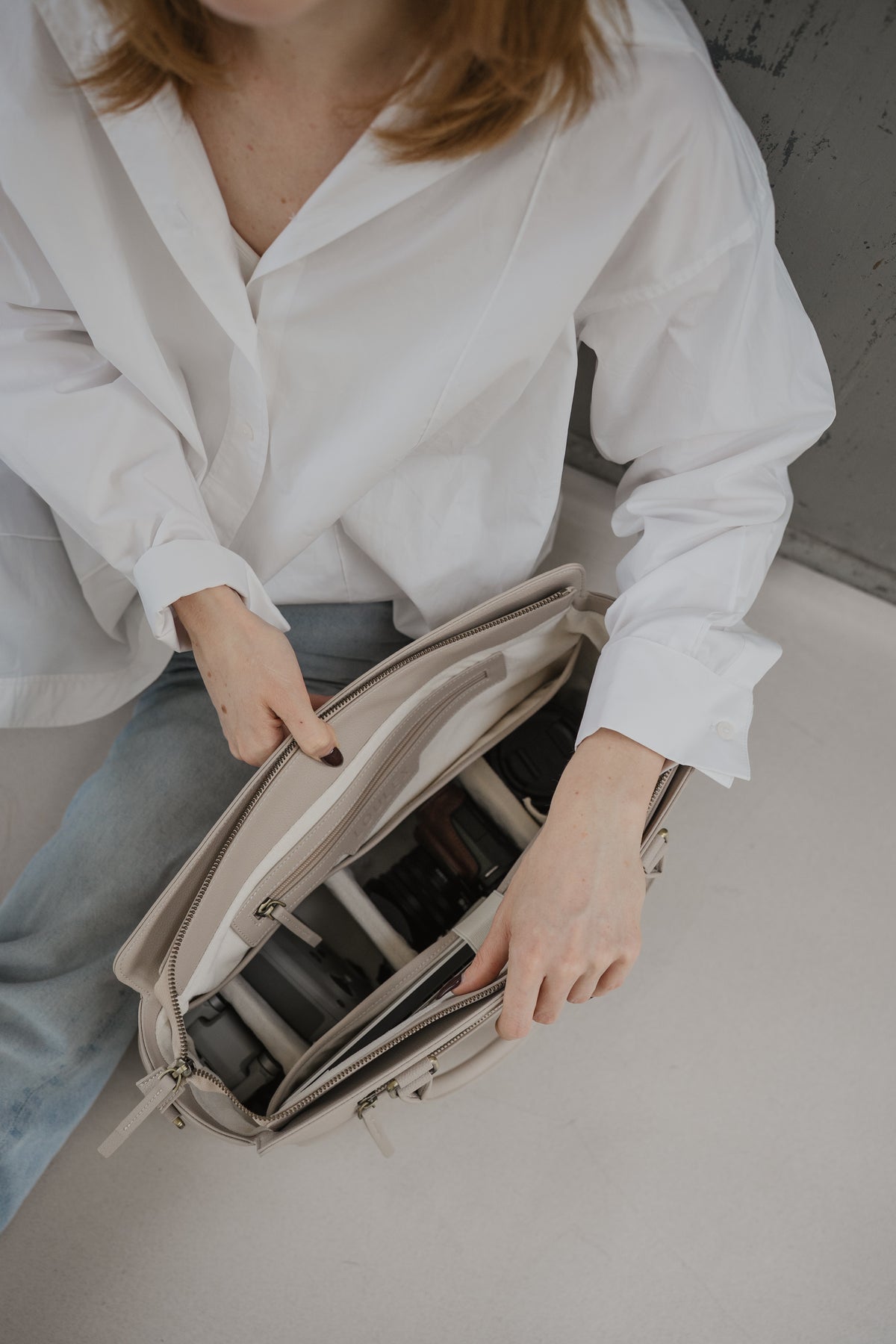 Person opening a beige travel bag on a light surface