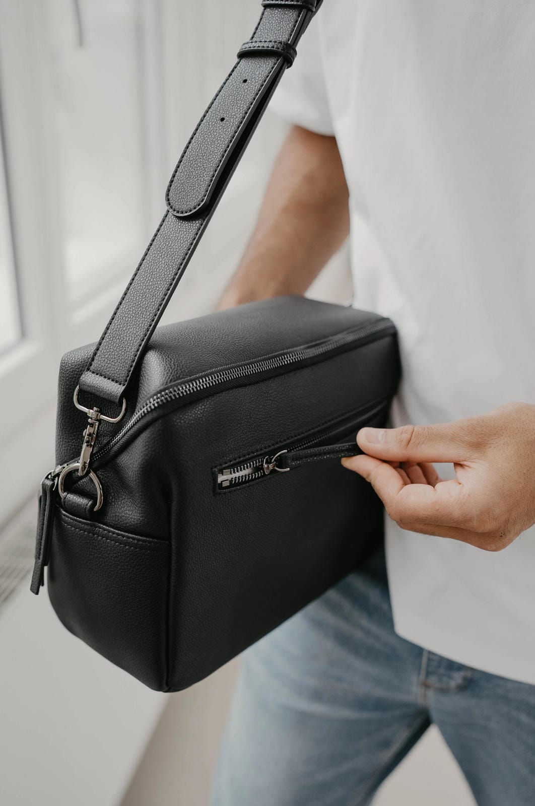 Person holding a black crossbody bag with a blurred background