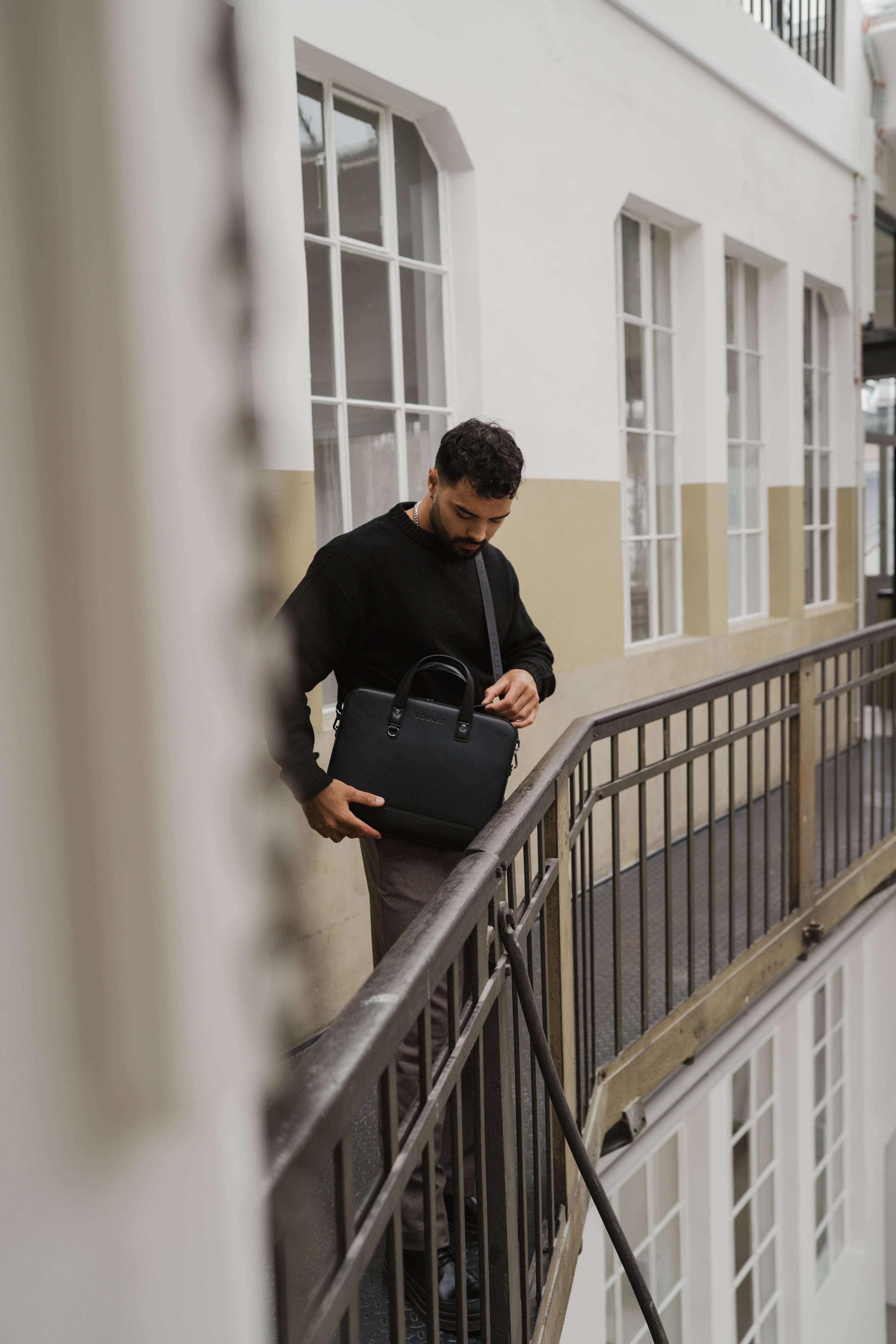 Man holding a black bag on a balcony with a building in the background