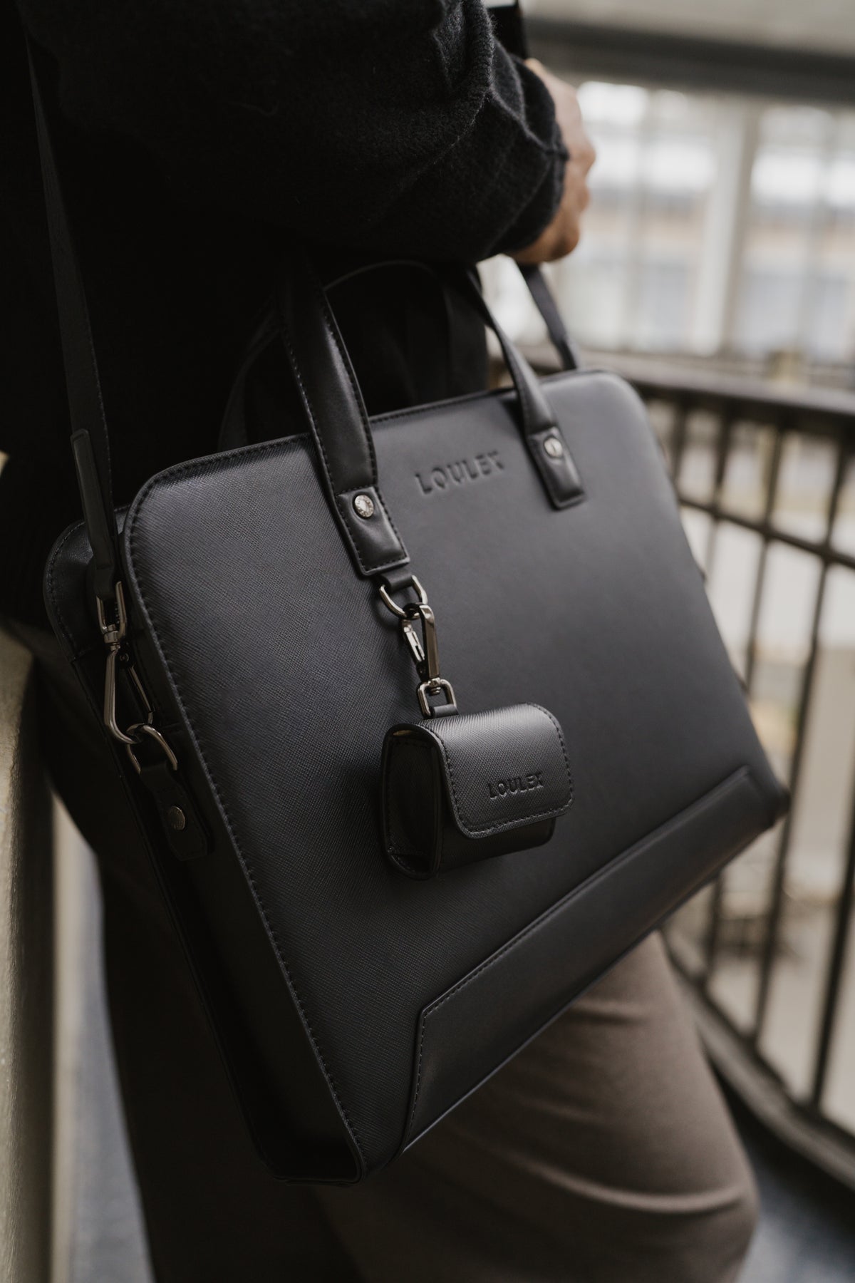 Black leather briefcase with visible brand logo held by a person outdoors.