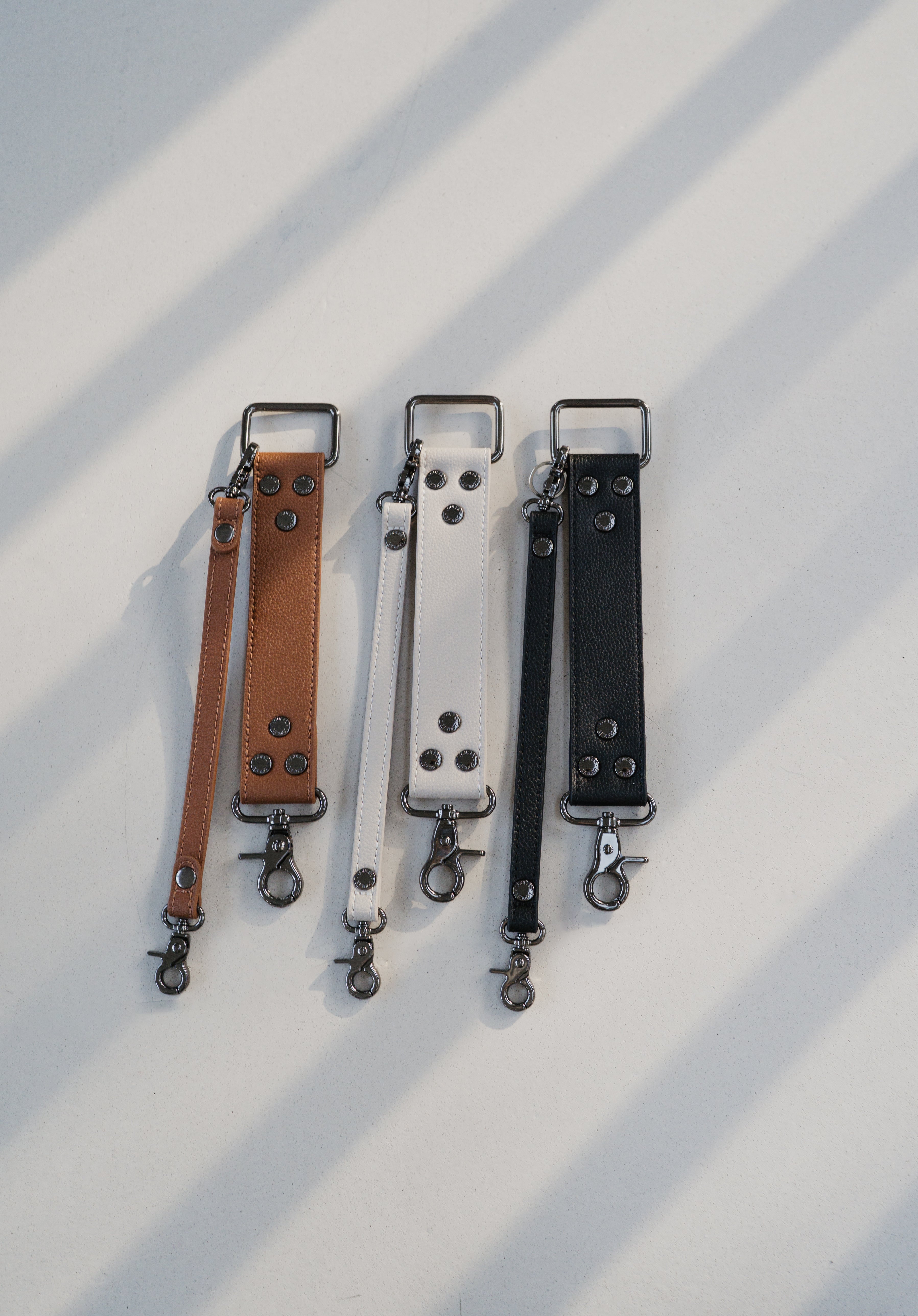 Three leather straps in brown, white, and black on a light background