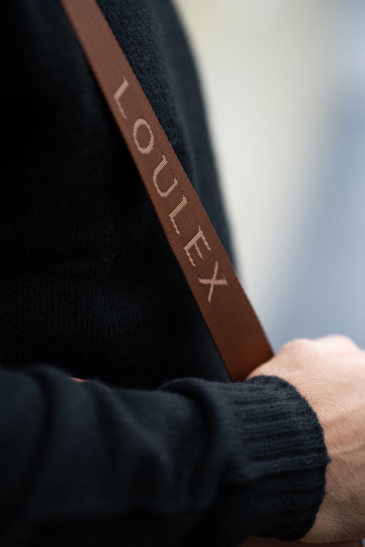 Brown strap with 'LOULEX' branding held by a person wearing a black sweater.