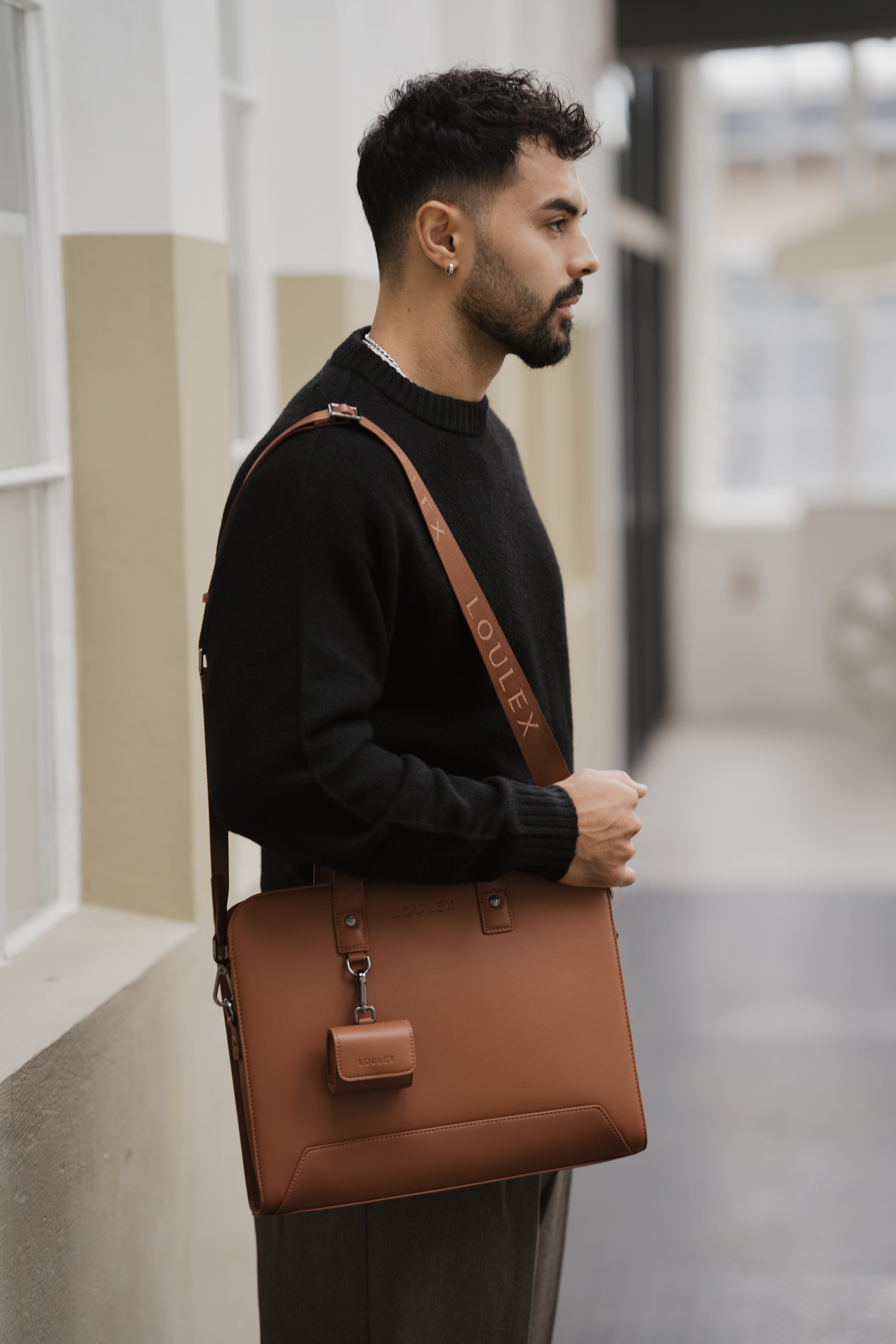 Man holding a brown leather bag in an indoor setting