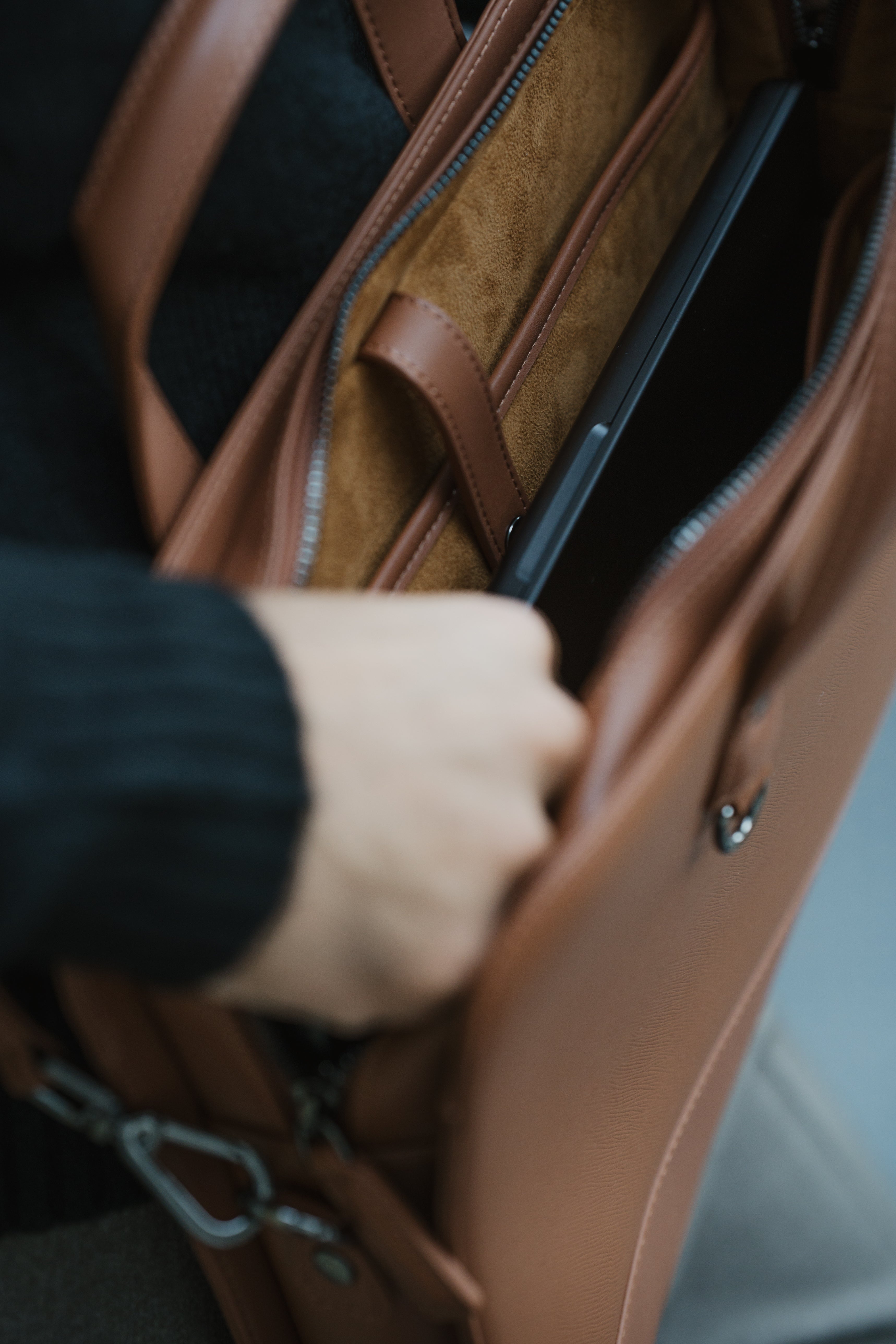 Person opening a brown leather bag with a hand reaching in