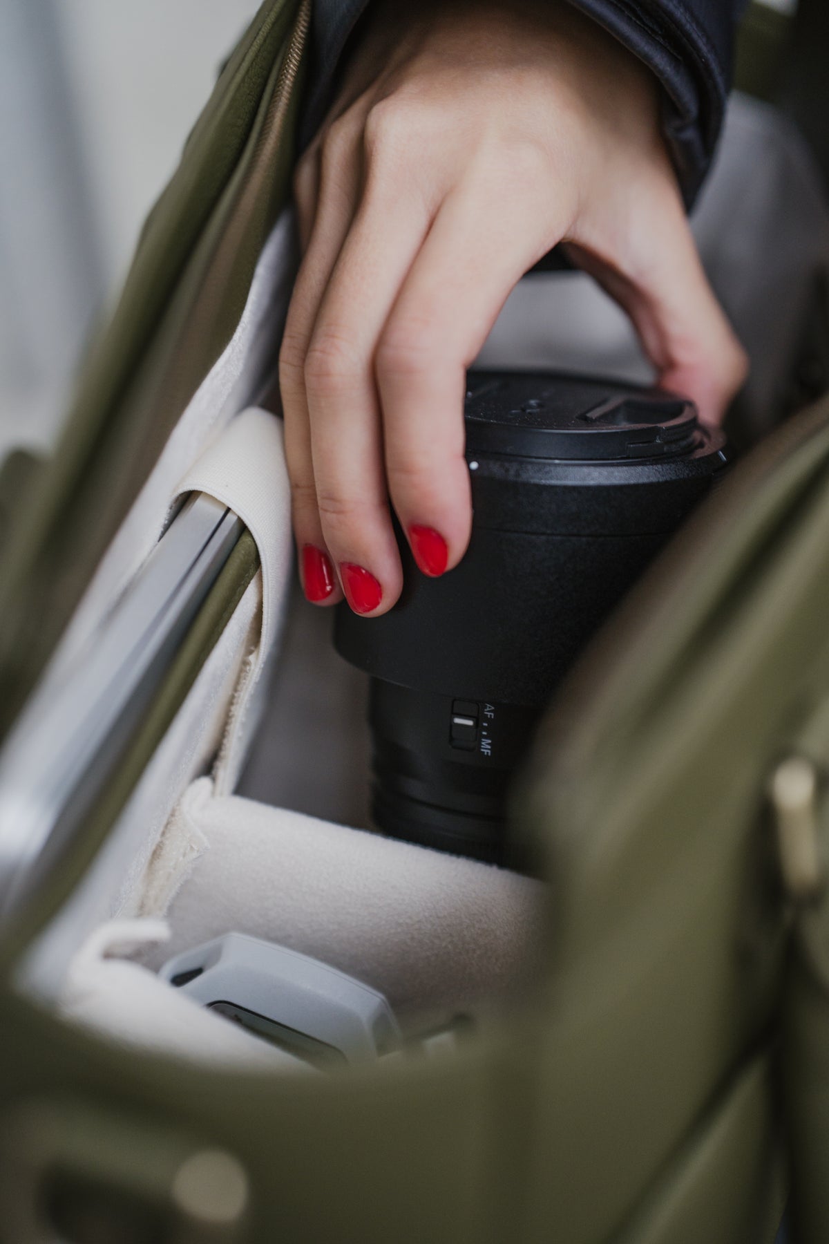 Hand with red nail polish holding a black coffee cup inside a car.