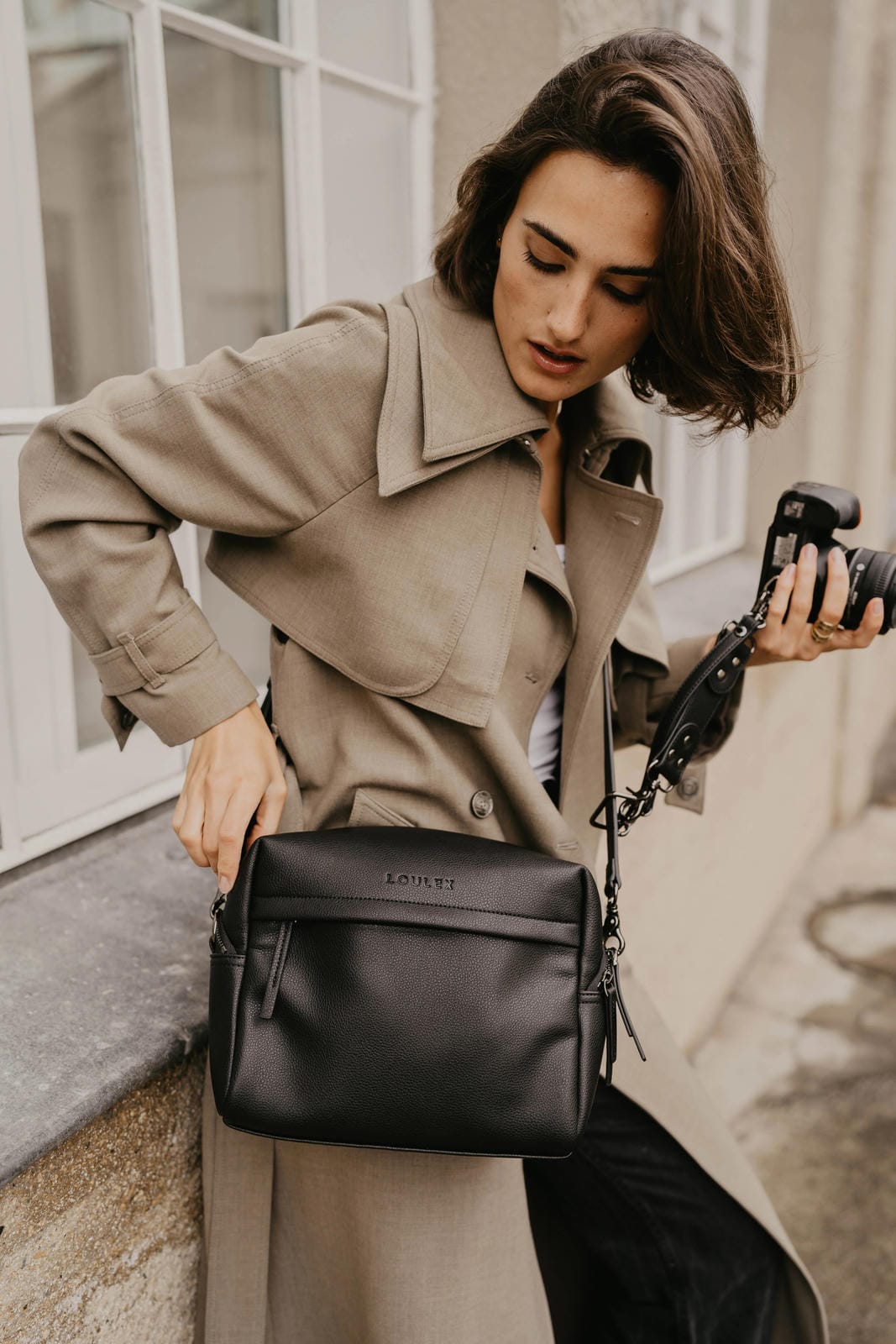 Woman holding a camera and a black handbag in an urban setting
