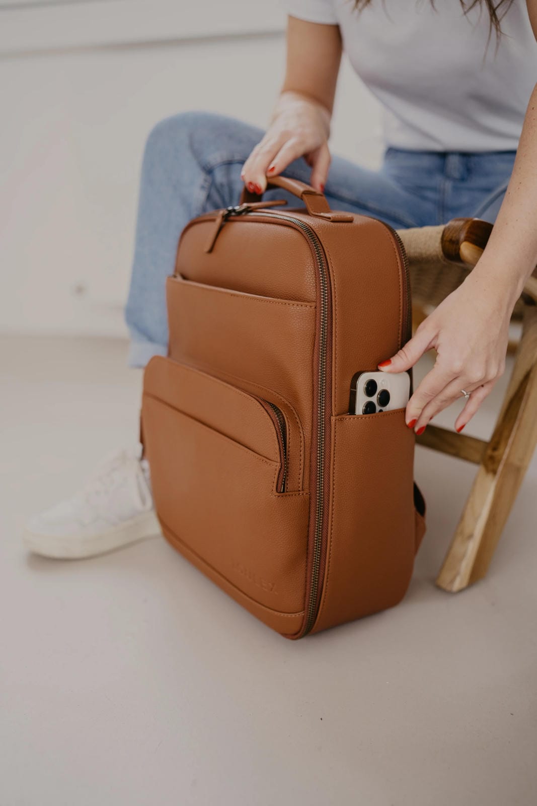 Person holding a brown leather backpack with a phone case on a light background