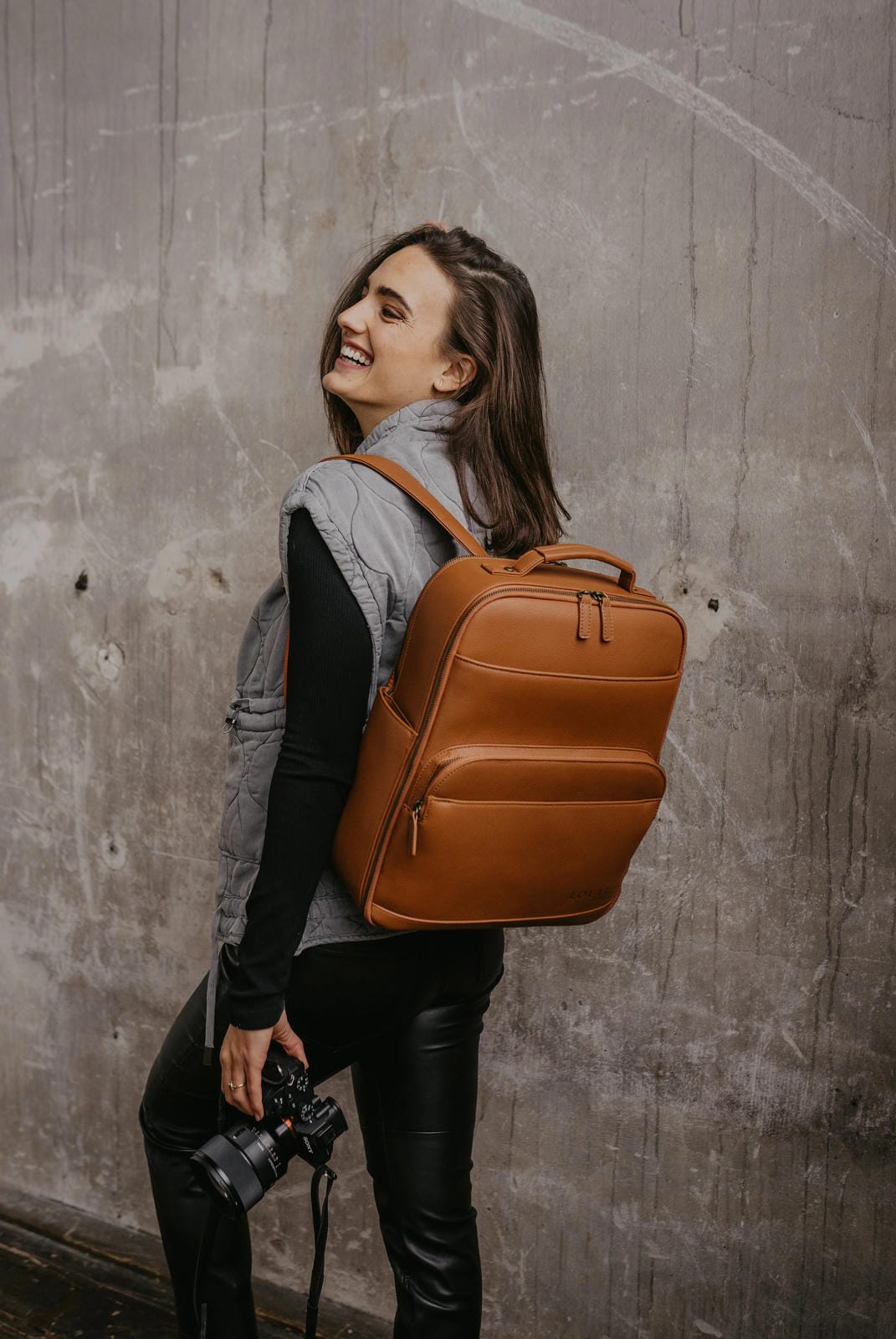 Woman with a brown backpack against a textured wall