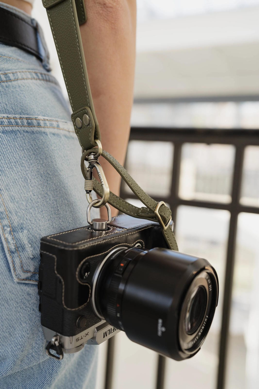 Camera with a strap held by a person wearing jeans, blurred background