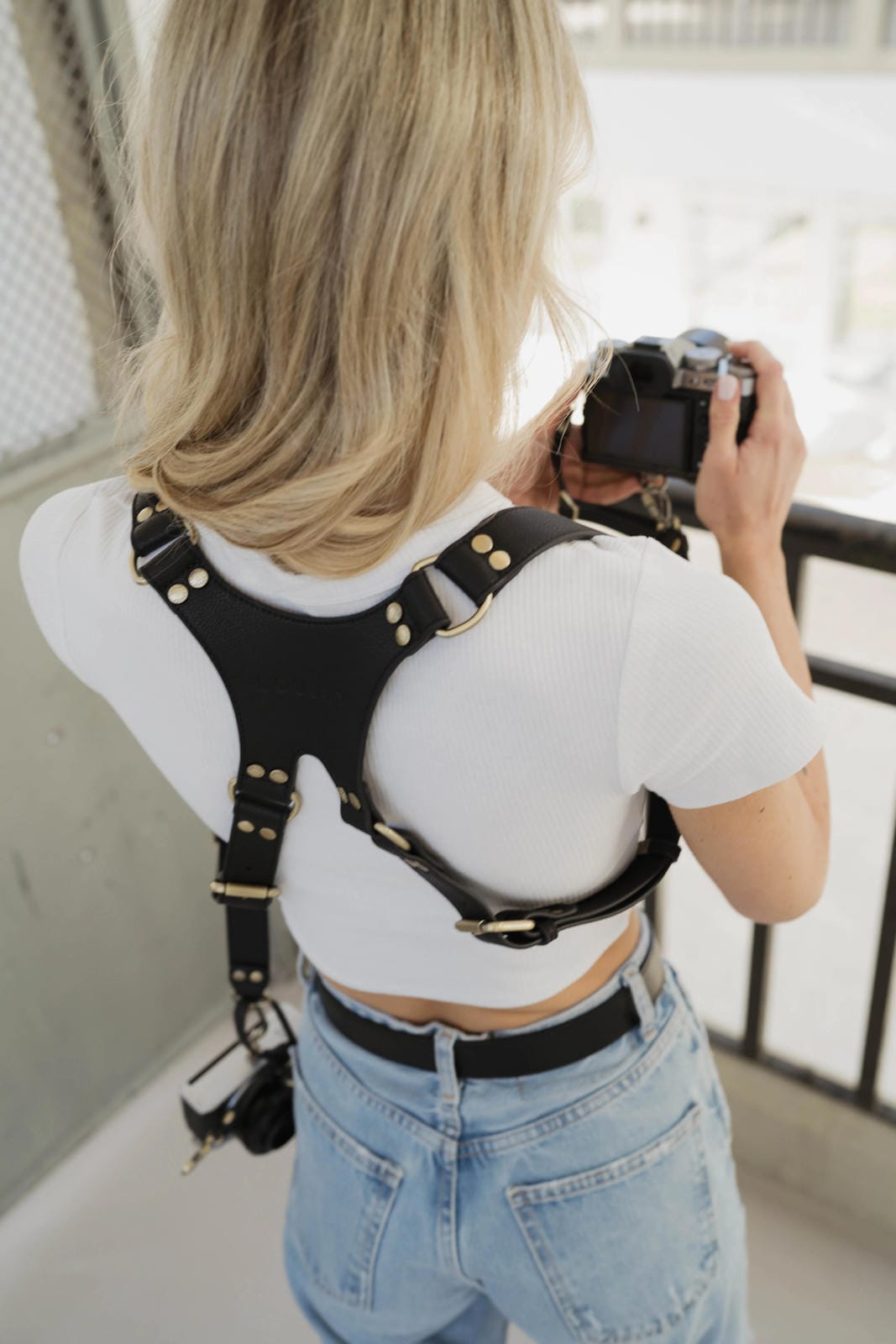 Person wearing a black camera harness holding a camera.