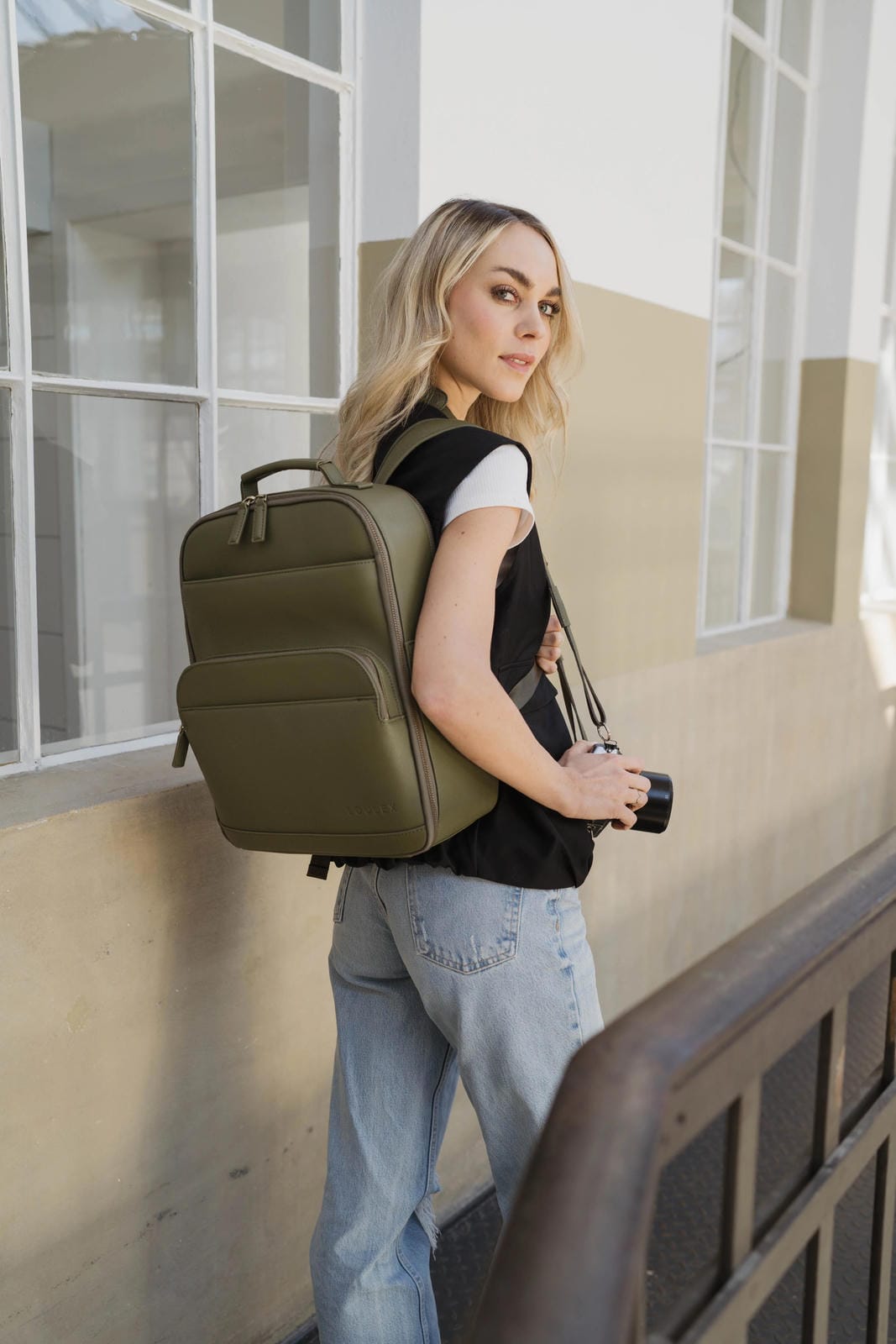 Woman with a green backpack standing against a building.