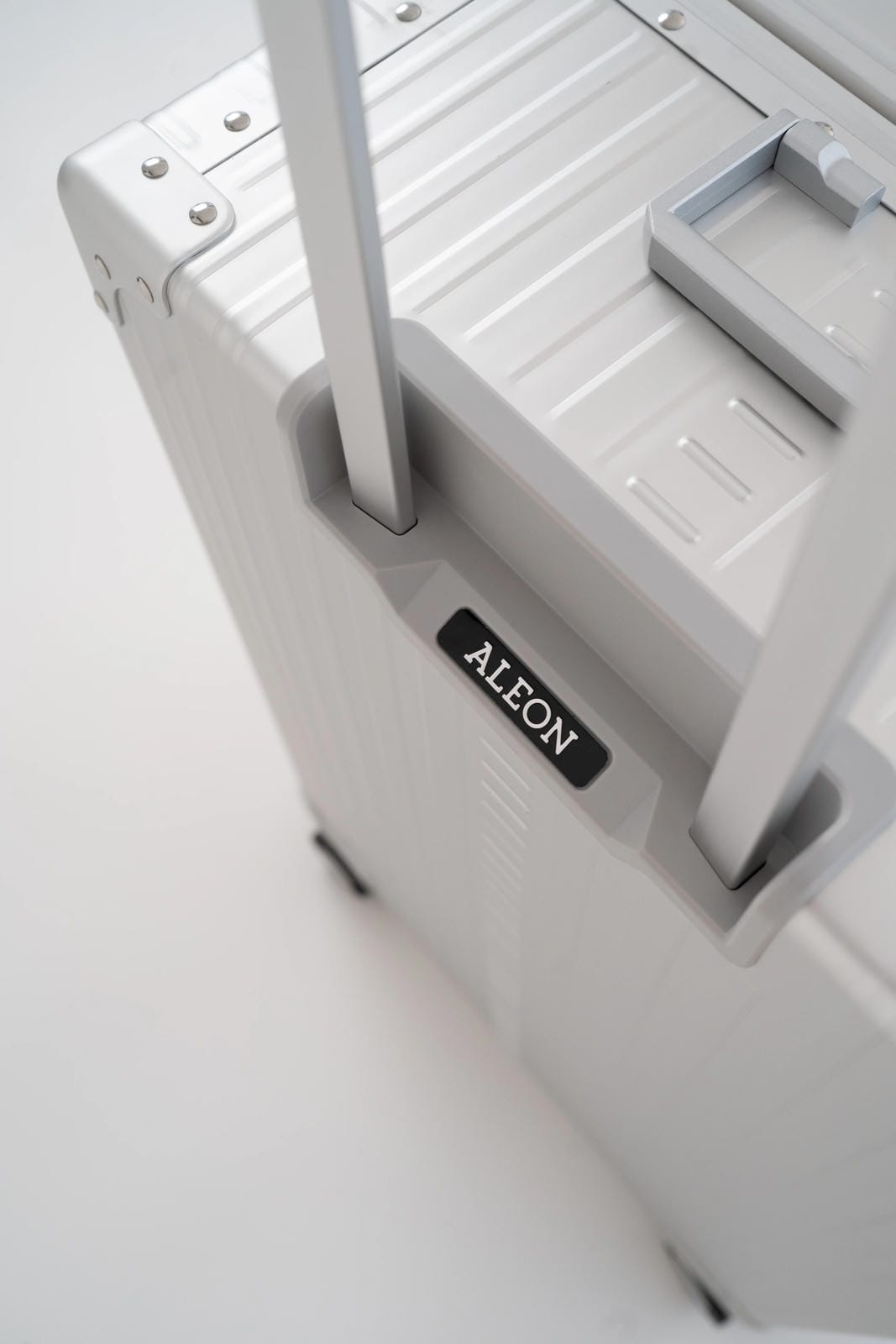 Close-up of a white suitcase with 'ALEON' branding on a light gray background