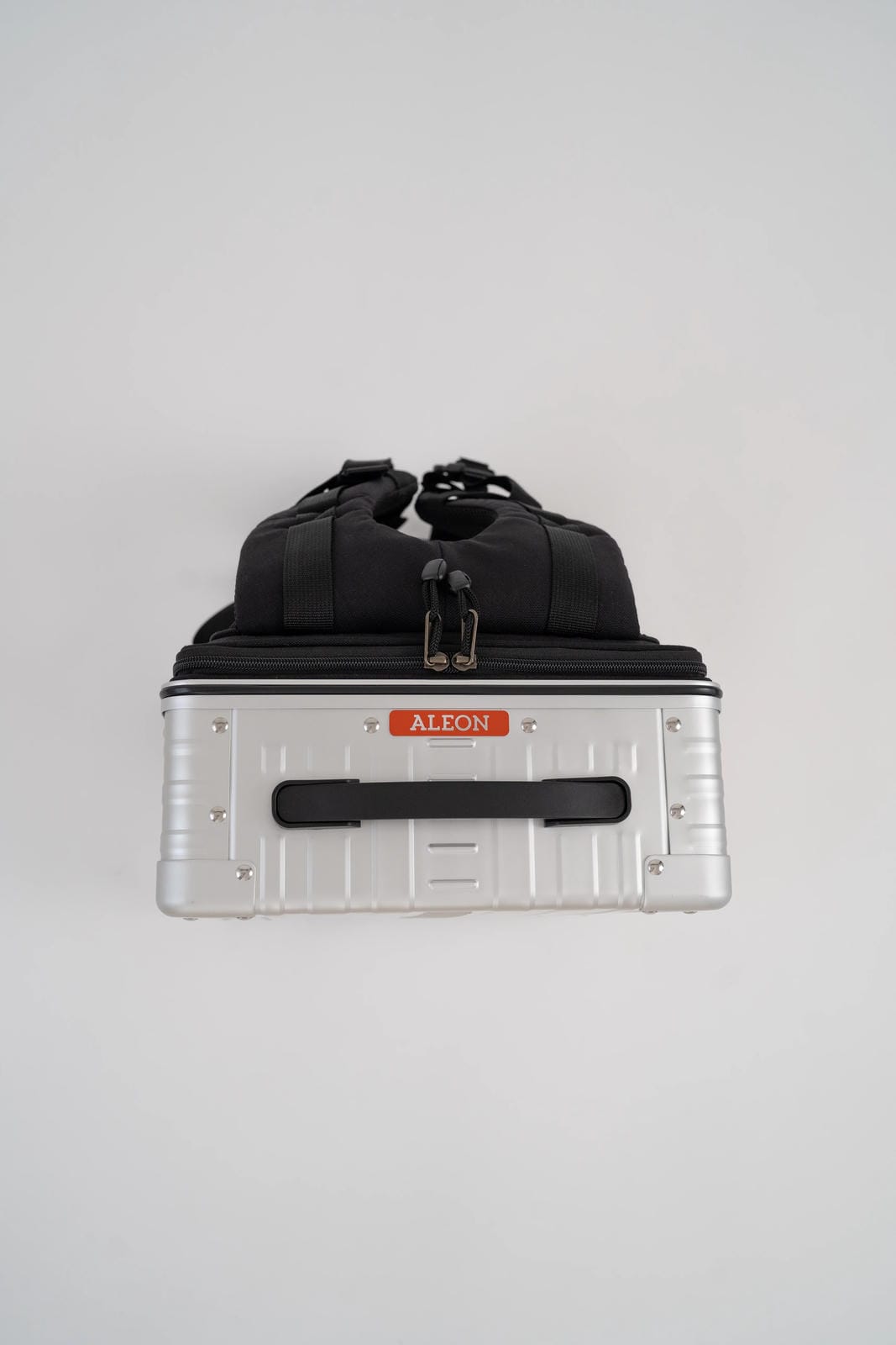 Black duffel bag on top of a silver toolbox with 'ALEON' branding on a light gray background
