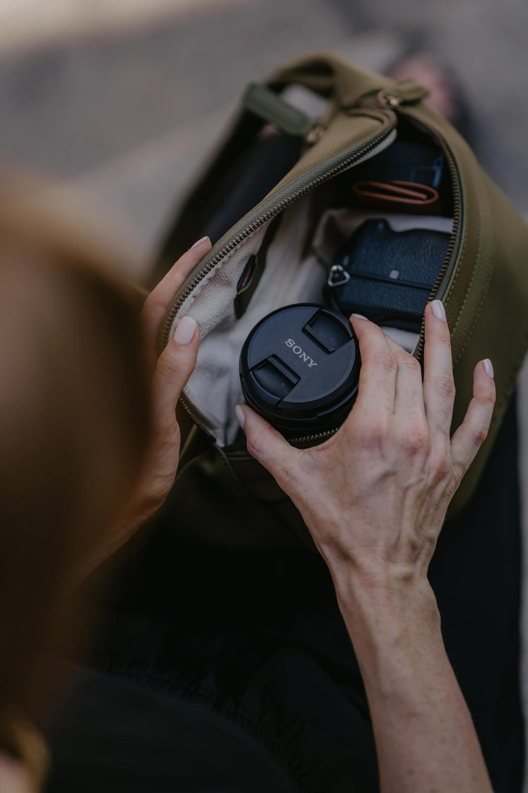 Person holding a Sony camera lens next to an open bag