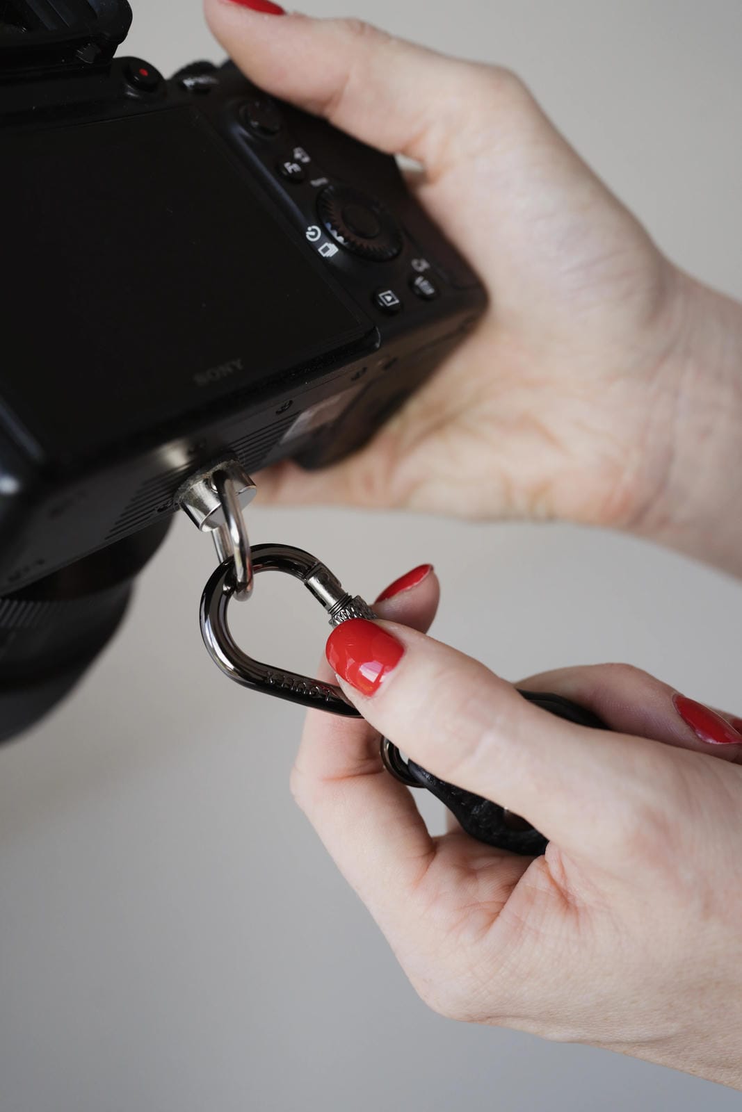 Person attaching a carabiner to a camera with a neutral background