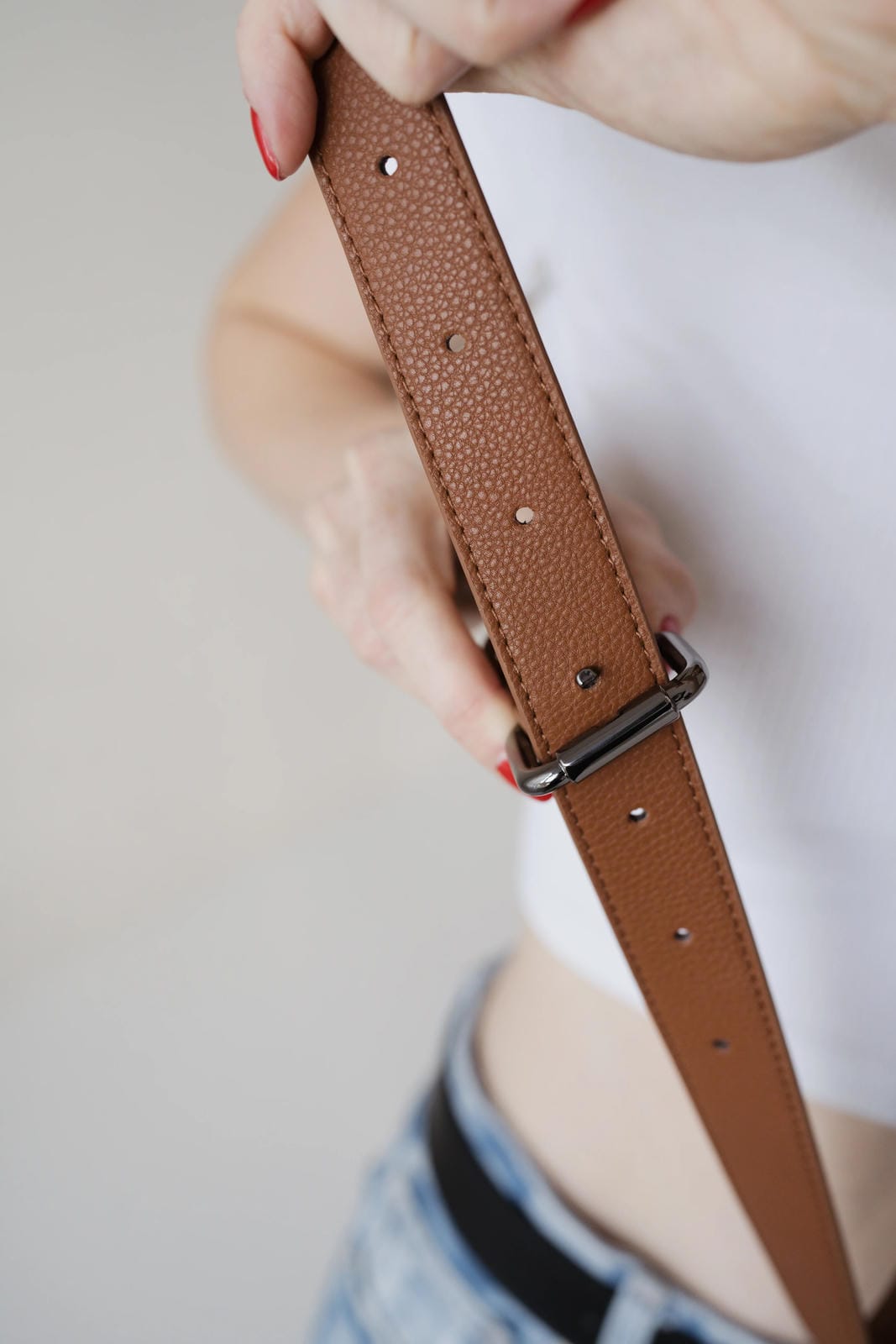 Brown leather belt held by a person against a neutral background