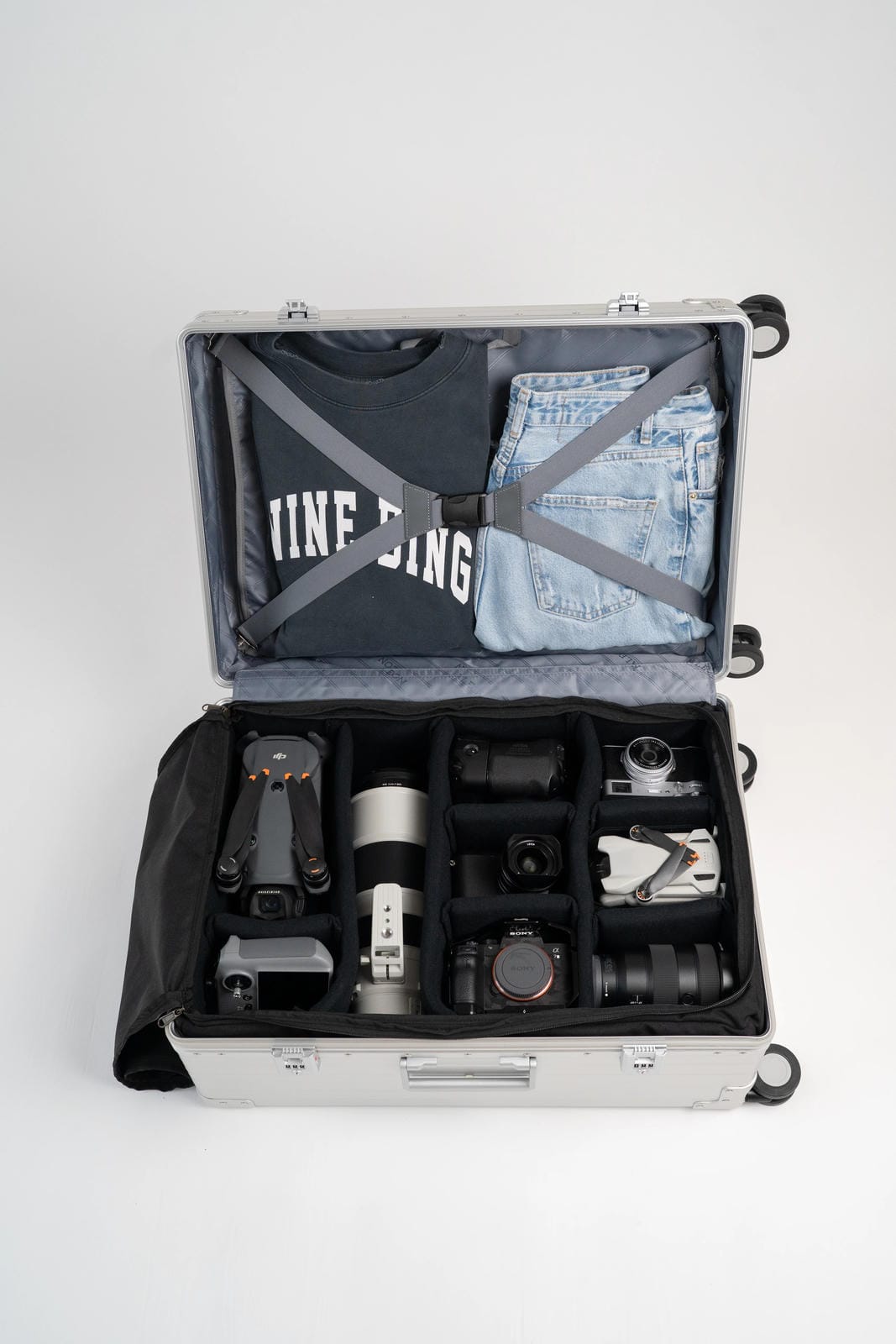 Open suitcase with camera equipment and clothing on a white background