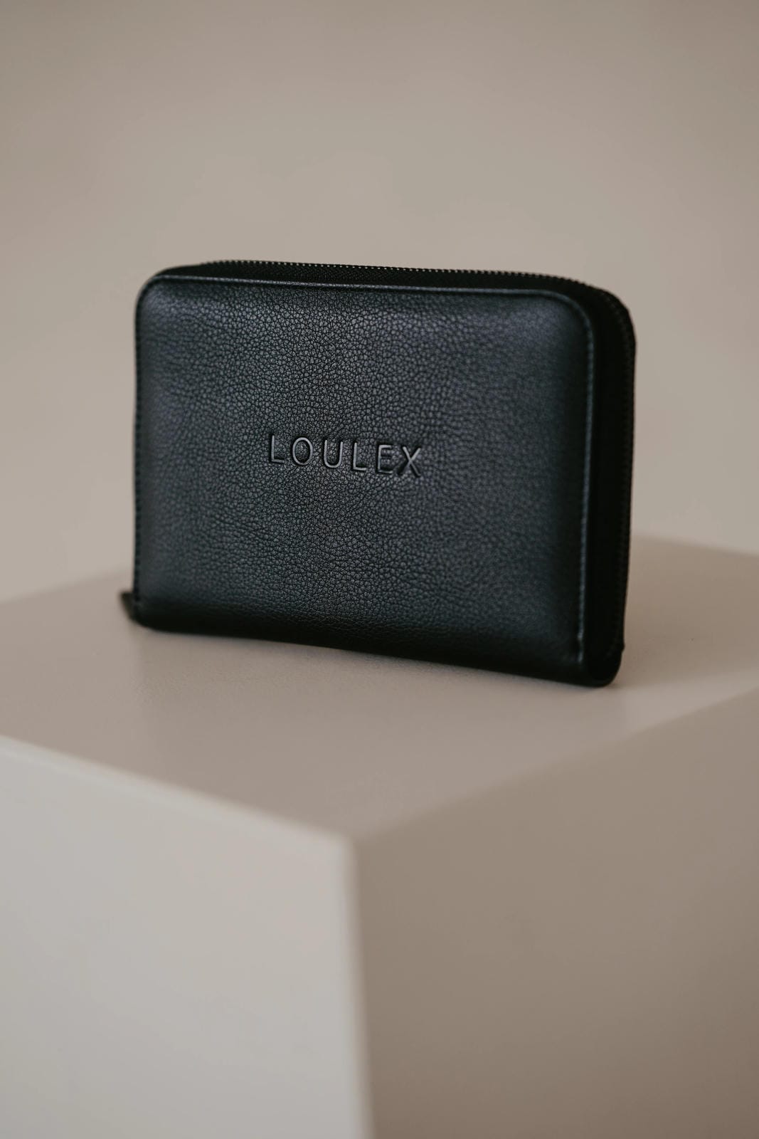 Black leather wallet with 'LOULEX' branding on a beige surface