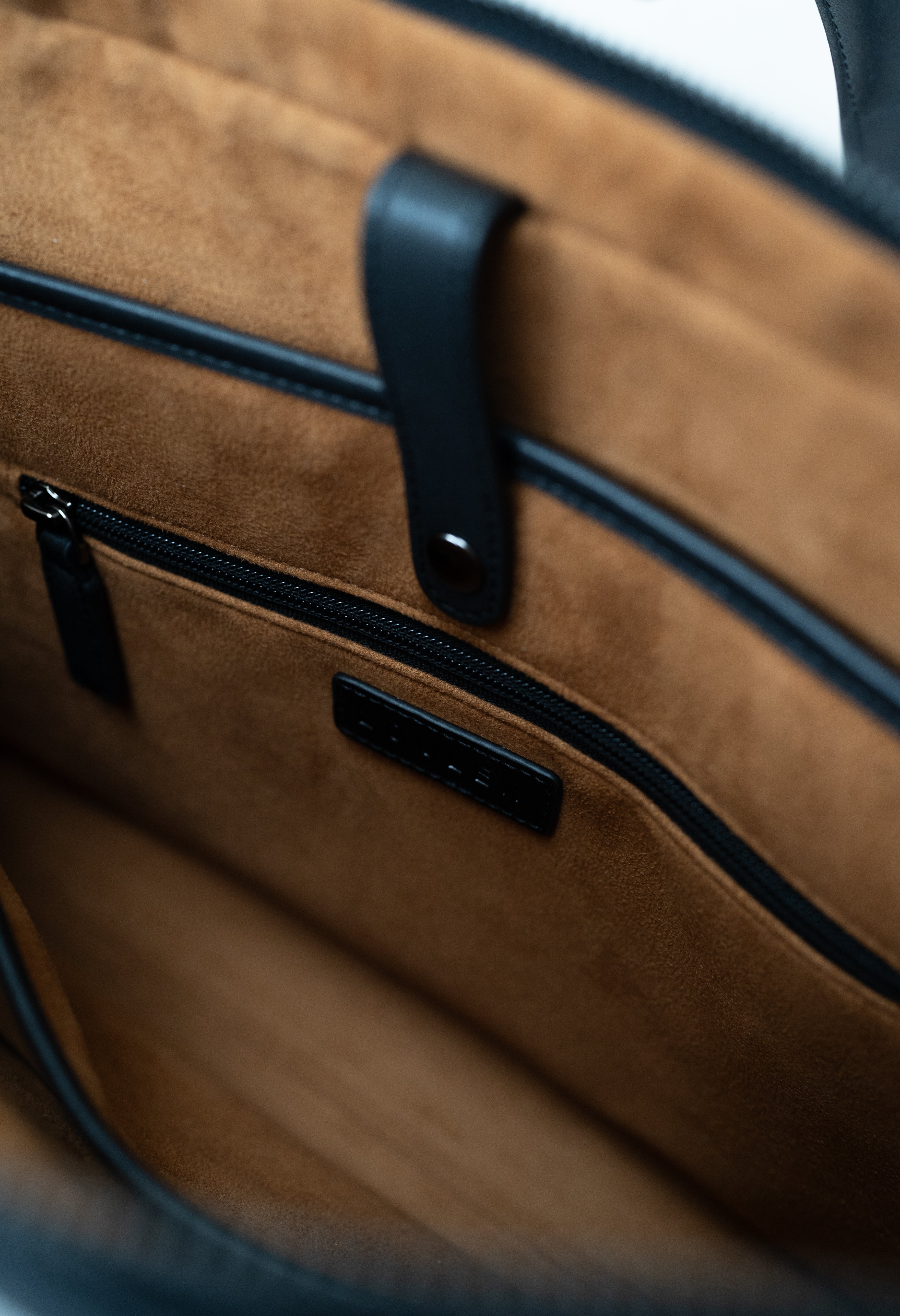 Close-up of a brown leather bag with black zipper and handle.