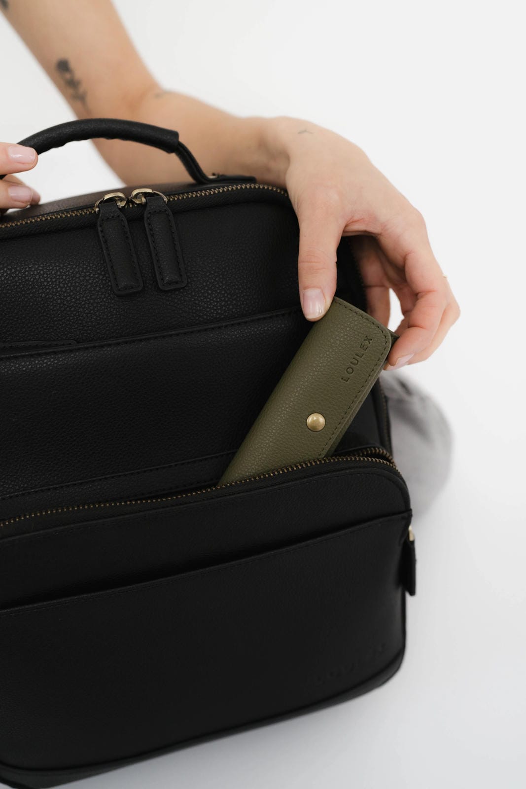 Black leather bag with a green strap held by a hand on a white background