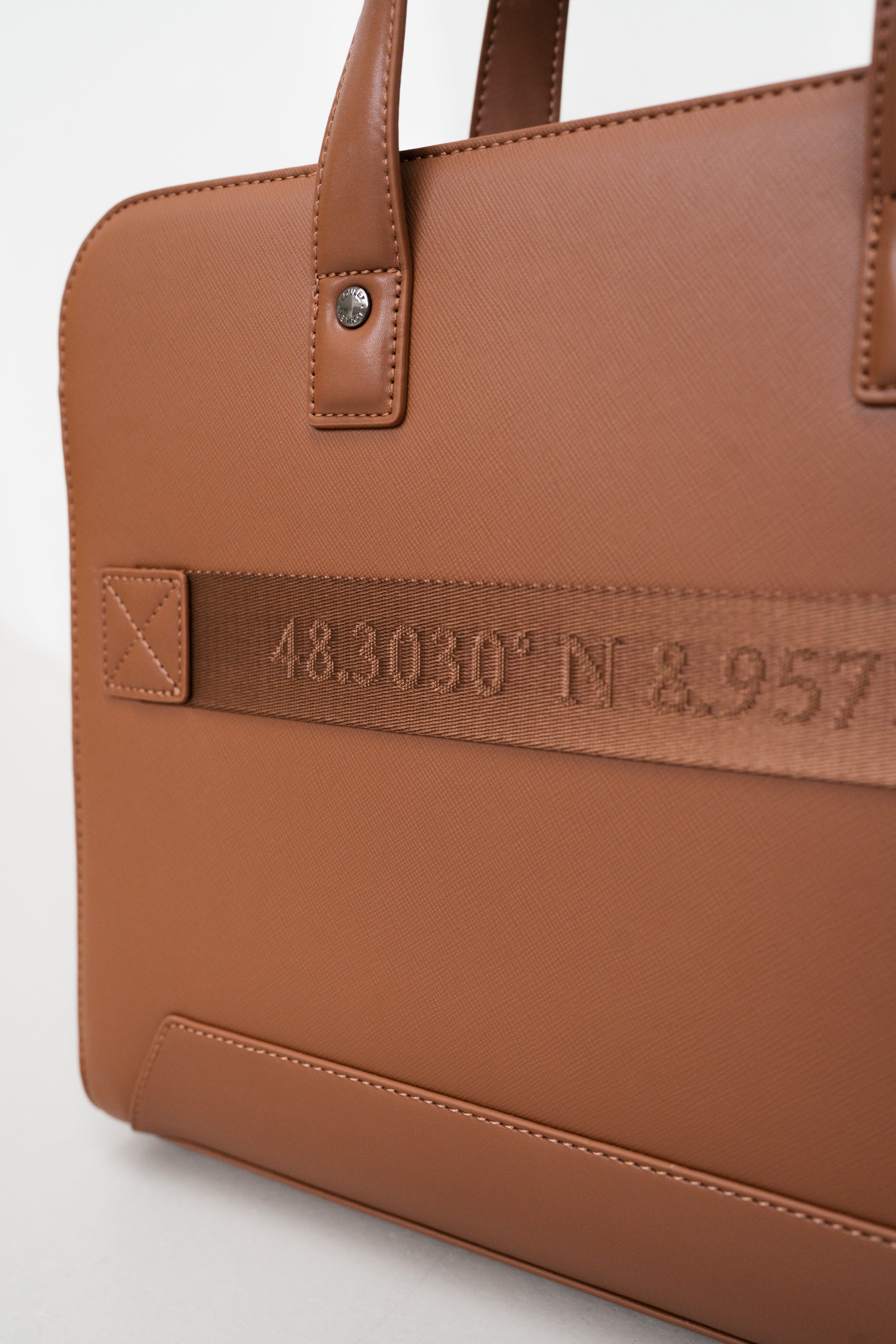 Brown leather bag with embroidered coordinates on a light gray background