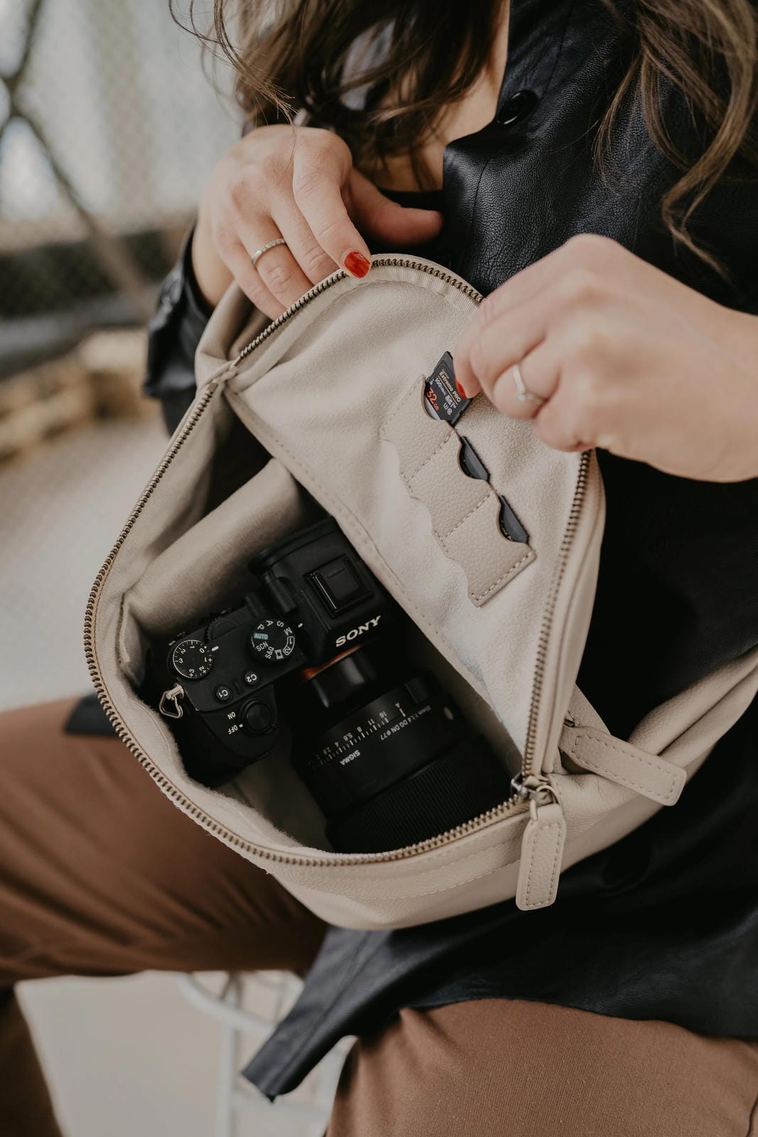 Person opening a beige bag to reveal a camera inside, with a blurred background.